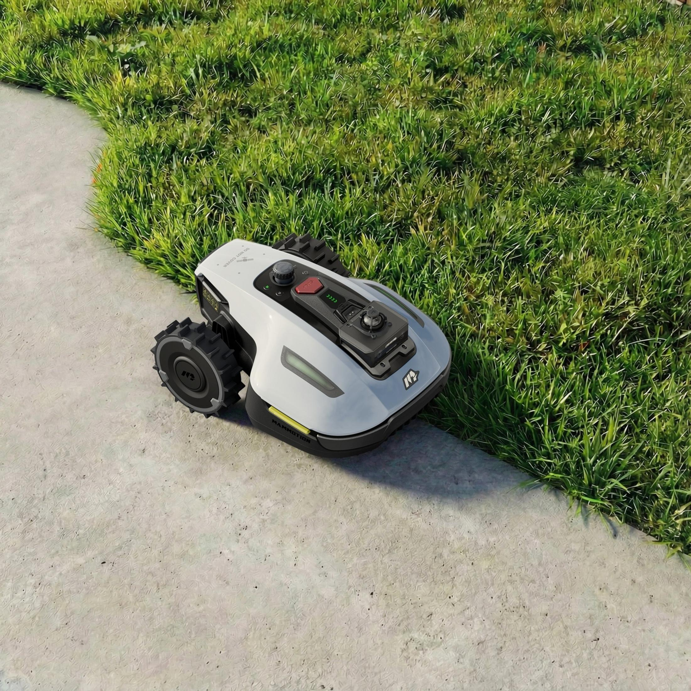 Un robot cortacésped blanco con ruedas negras está en un camino de cemento junto a la hierba.