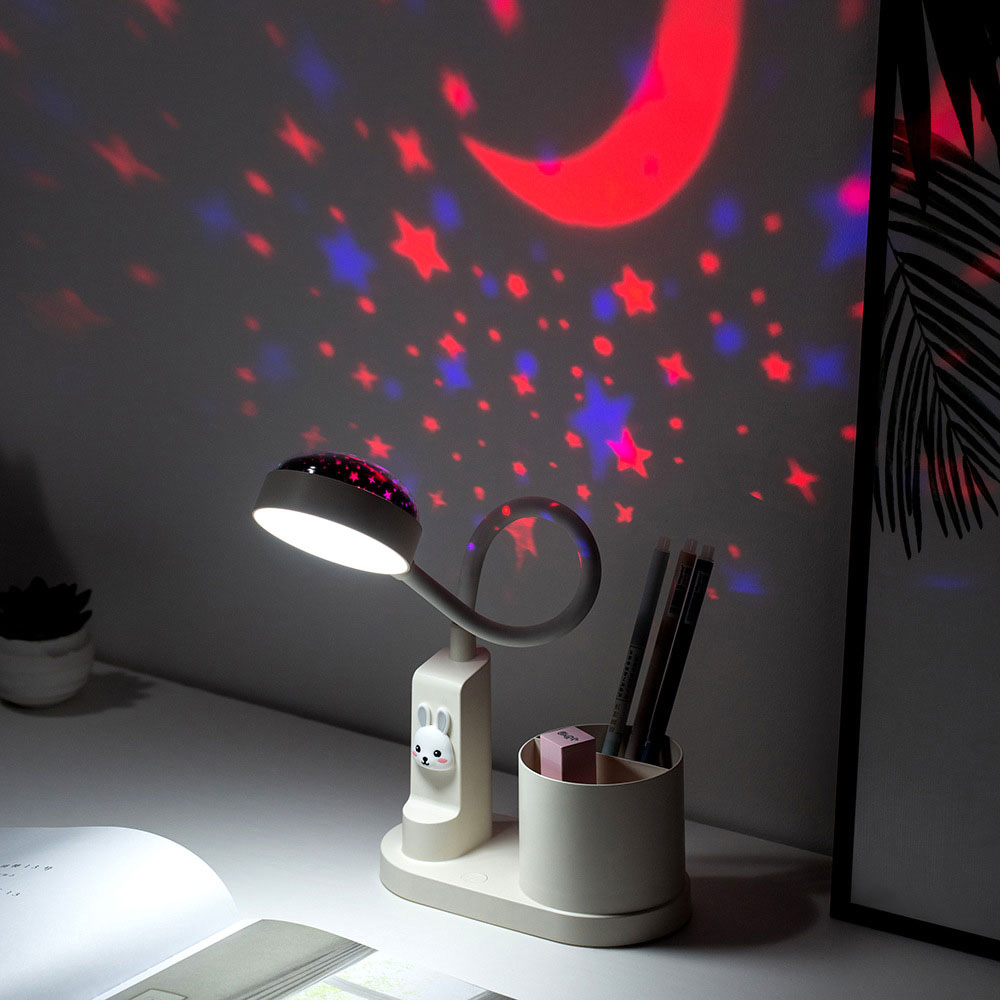 Ein Nachttischlampen-Projektor wirft rote und blaue Sterne und einen Mond.