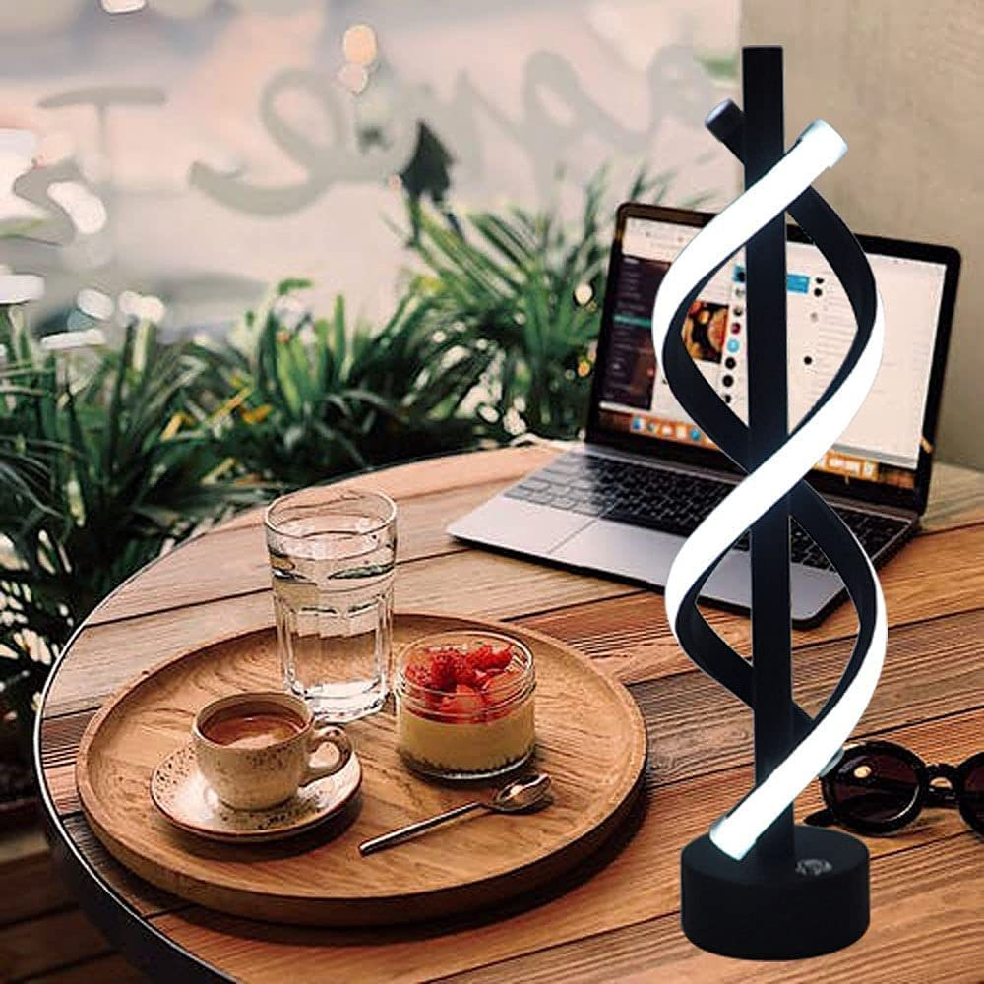 Ein moderner Schreibtisch mit einer verdrehten Lampe, Laptop, Kaffee und Dessert.