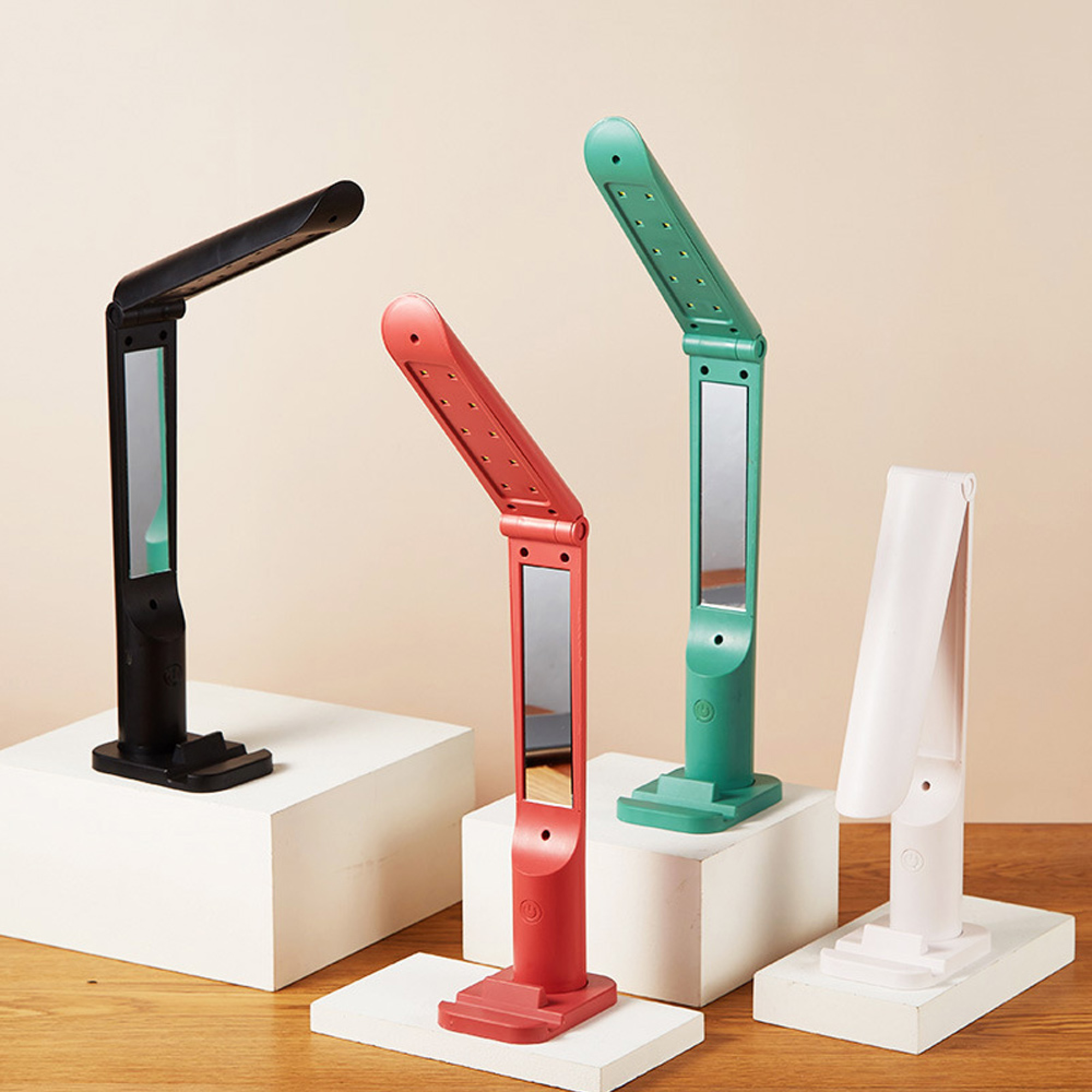 Vier zusammenklappbare LED-Lampen in Schwarz, Rot, Grün und Weiß auf weißen Podesten.