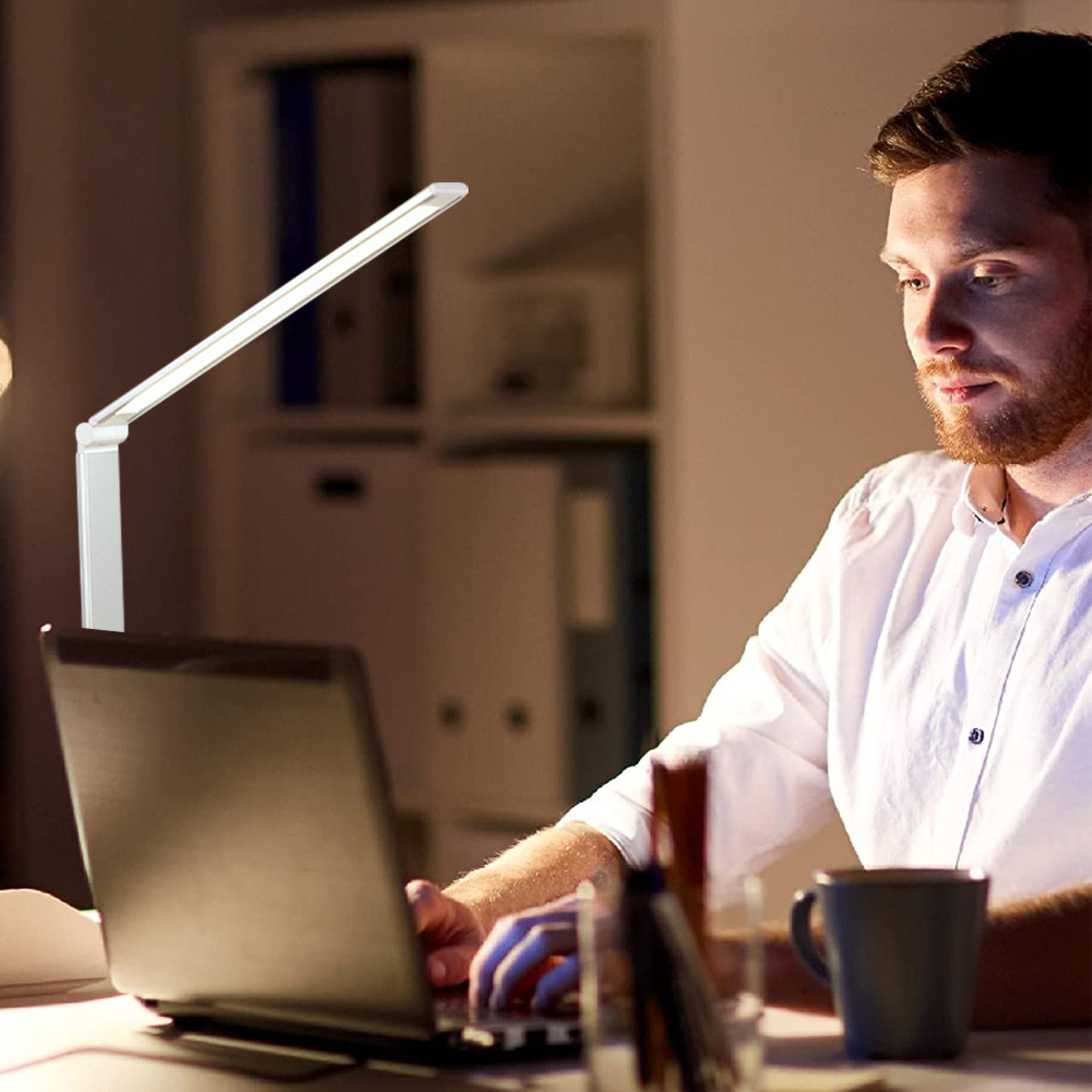 Ein Mann mit Bart arbeitet nachts am Laptop, beleuchtet von einer Schreibtischlampe.