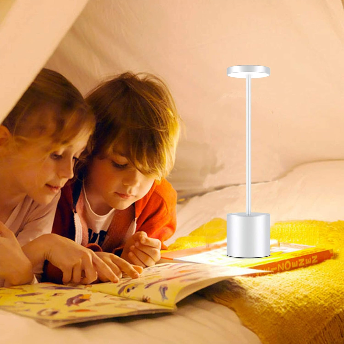 Zwei Kinder lesen ein Buch, beleuchtet von einer kleinen Tischlampe.