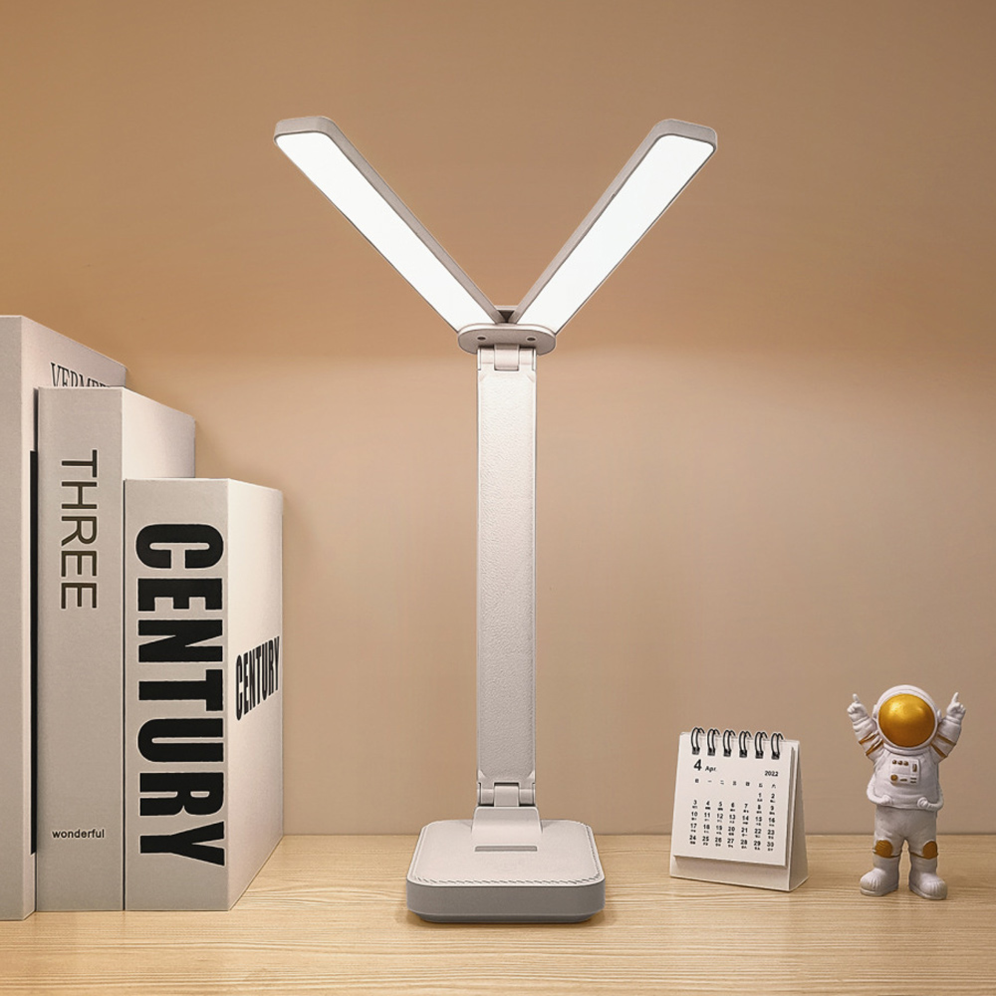 Ein weißer Schreibtisch mit einem silbernen V-förmigen LED-Licht, Büchern und einer Astronautenfigur.