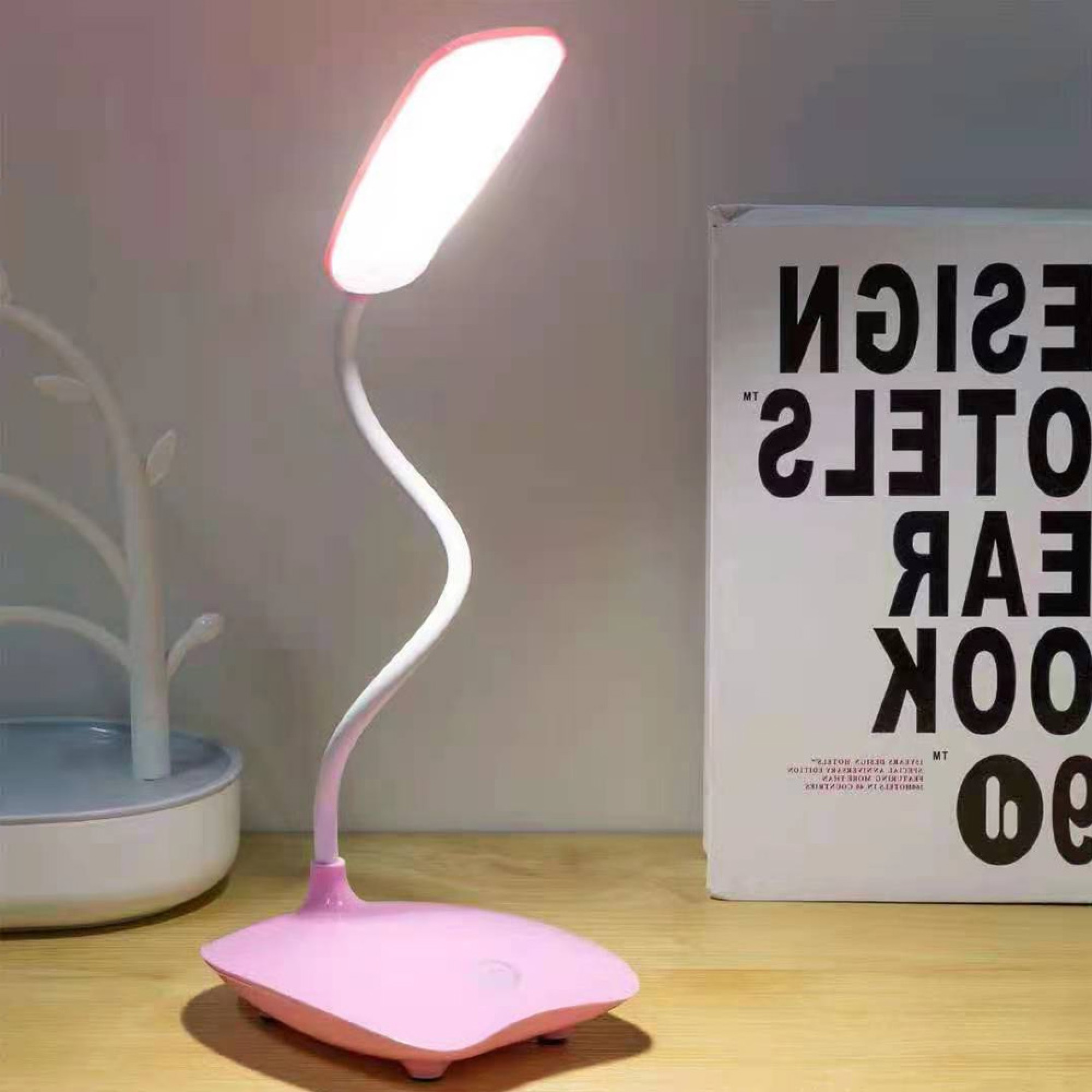 Ein rosa Schreibtischlampe mit biegsamem Hals steht neben einem Buch.