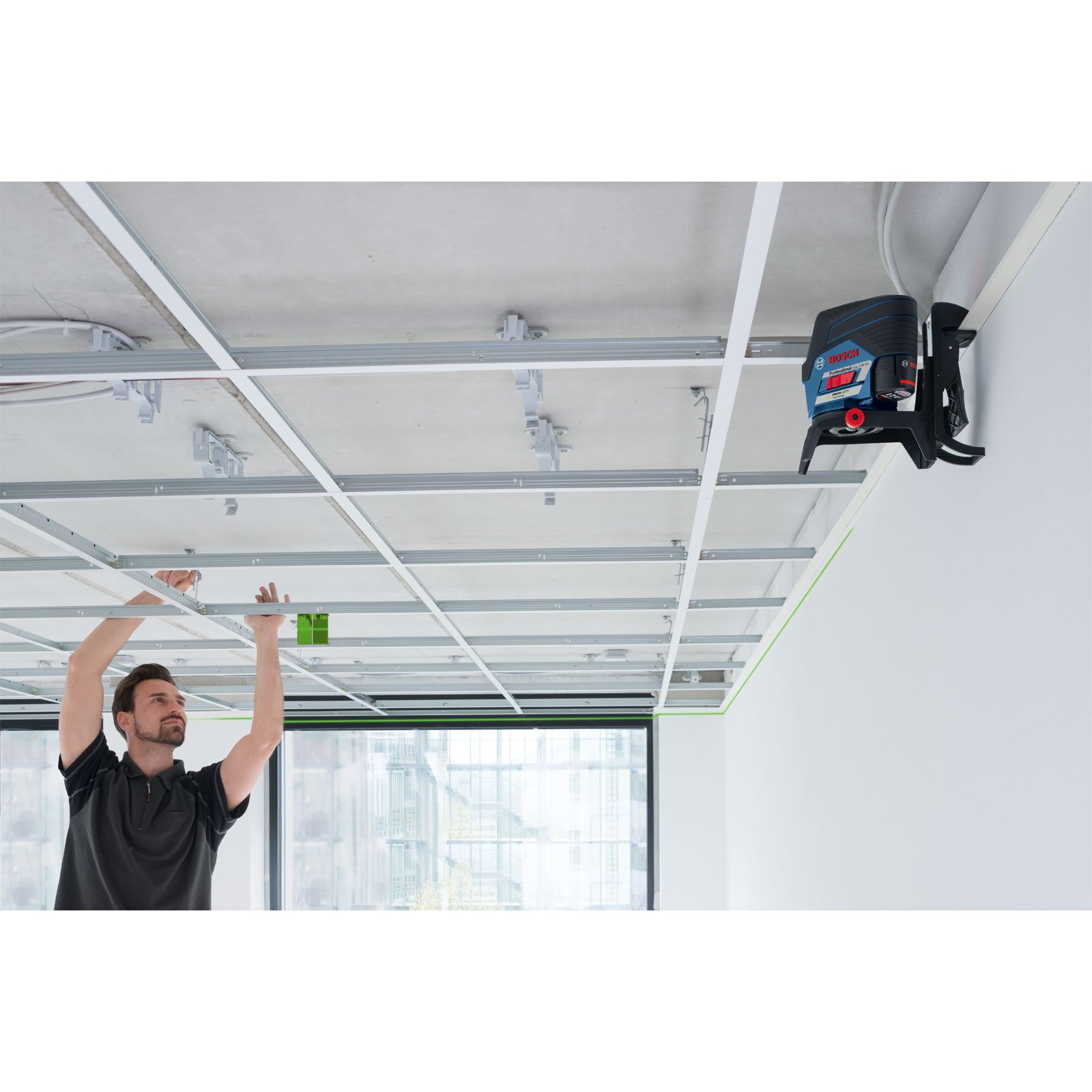 Ein Mann installiert eine abgehängte Decke mit einem Lasernivellierer und Schienensystem.