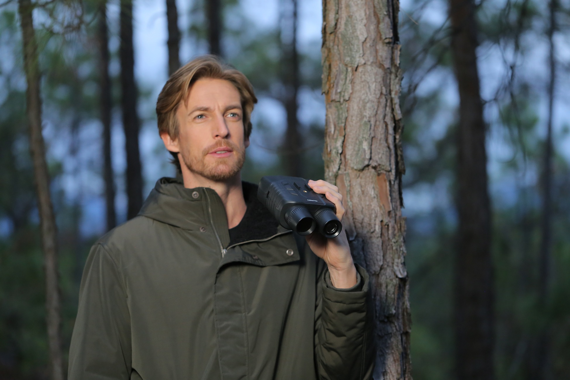 Mann im Wald hält Fernglas.
