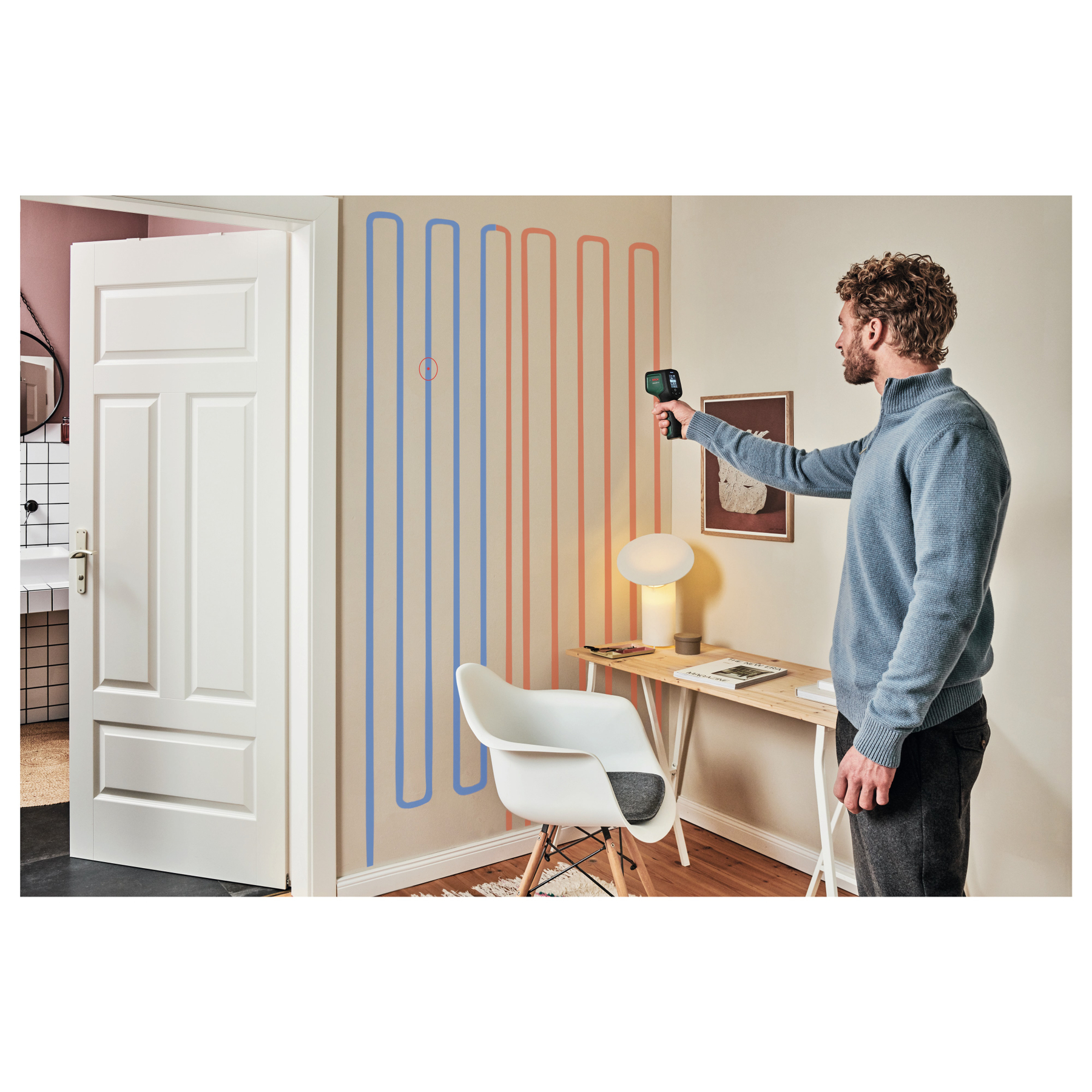 Mann misst Wand mit Thermometer, blaue und rote Linien an Wand.