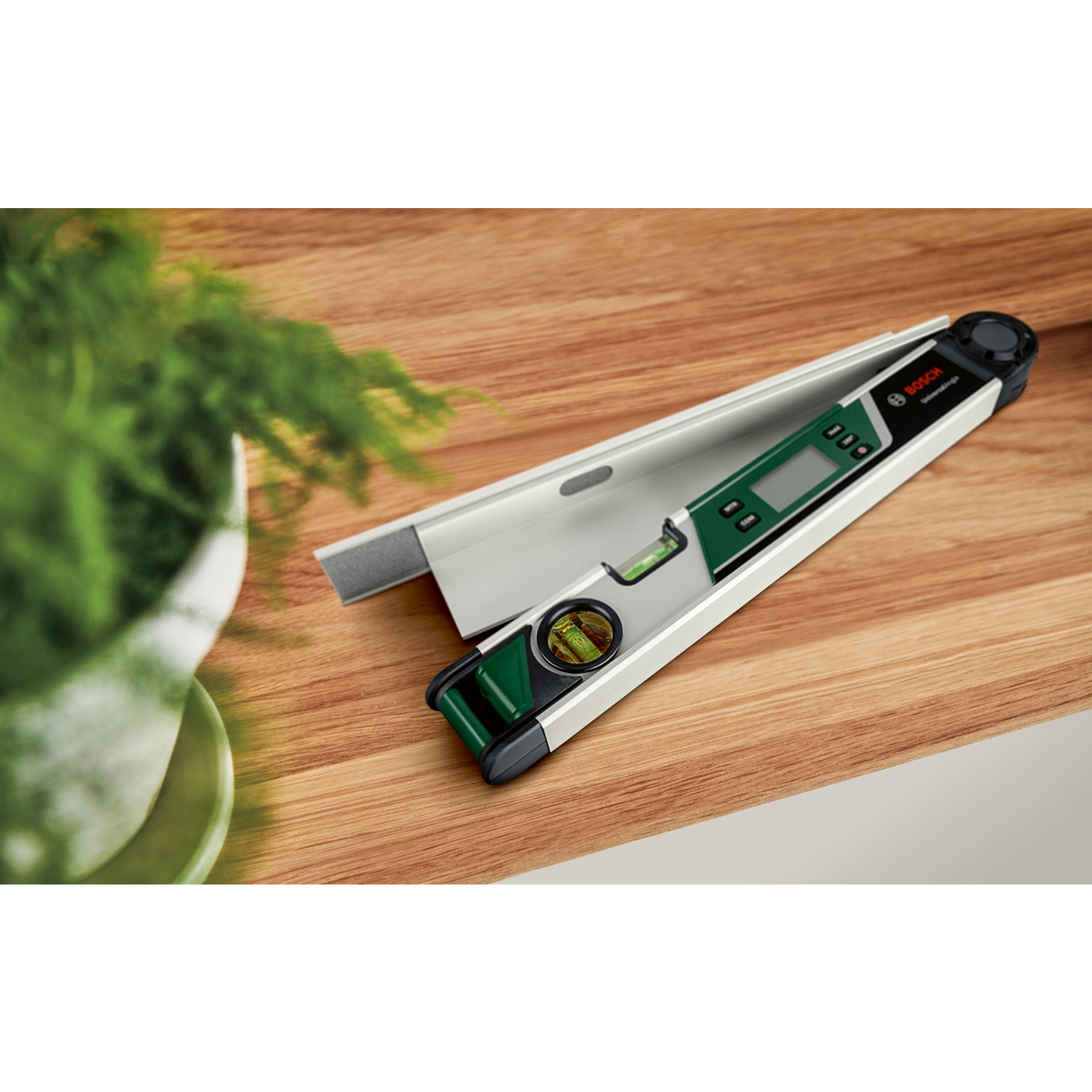 Ein Bosch Digital-Winkelmesser liegt auf einem Holzbrett neben einer Topfpflanze.