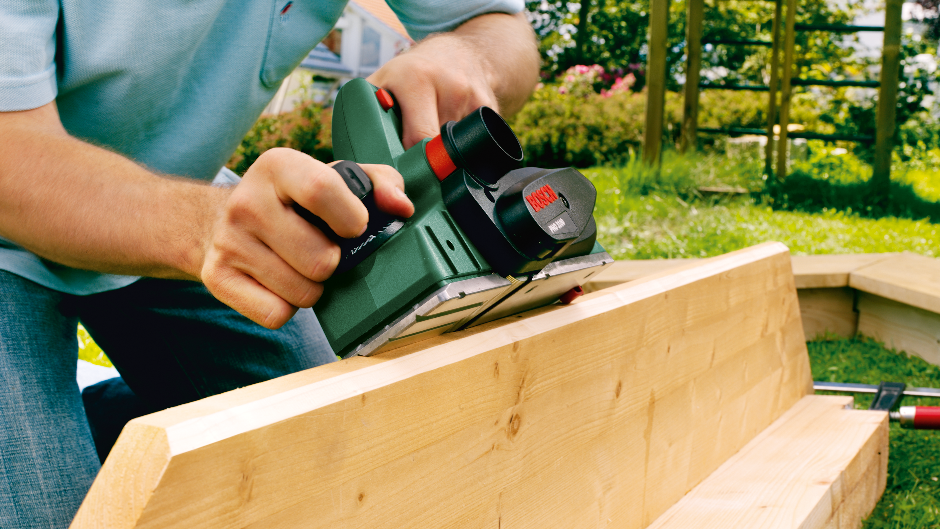 Mann bearbeitet Holz mit Hobel im Garten.