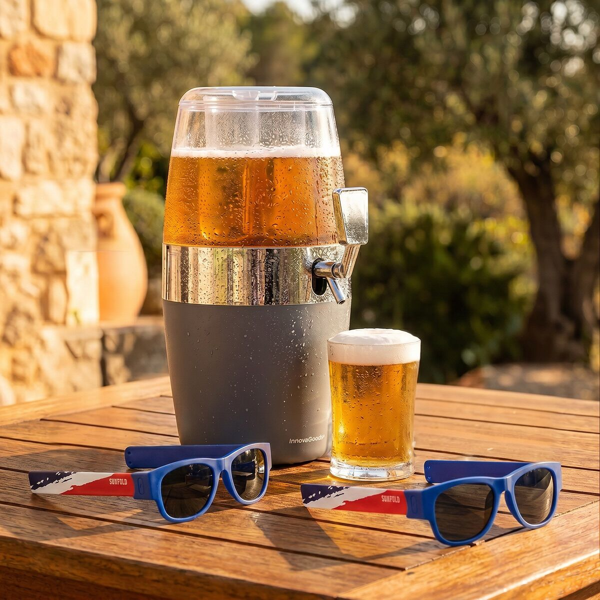Bierdispenser, ein Glas Bier und Sonnenbrillen auf einem Holztisch im Freien.