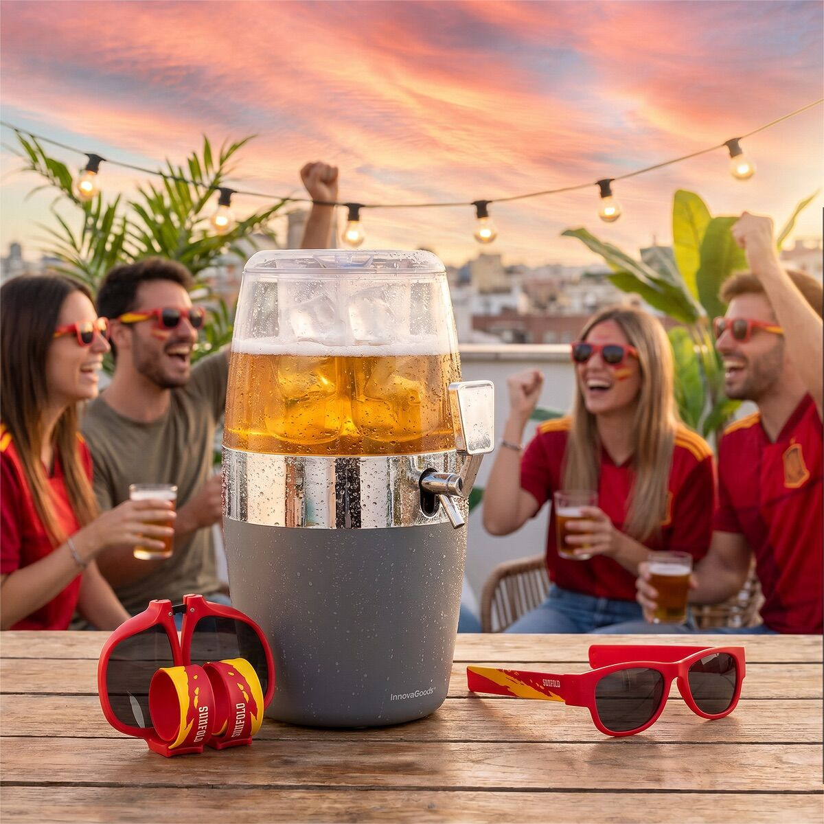 Quattro persone in maglie spagnole tifano con birra su un tetto al tramonto. Dispenser di birra sul tavolo.