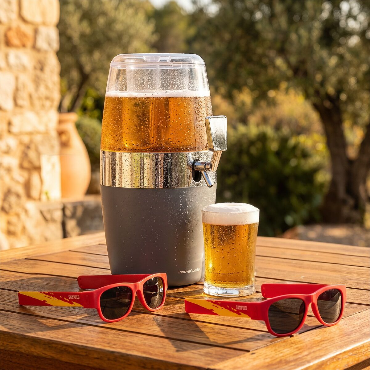 Dispenser di birra con bicchiere e due occhiali da sole su tavolo legno.