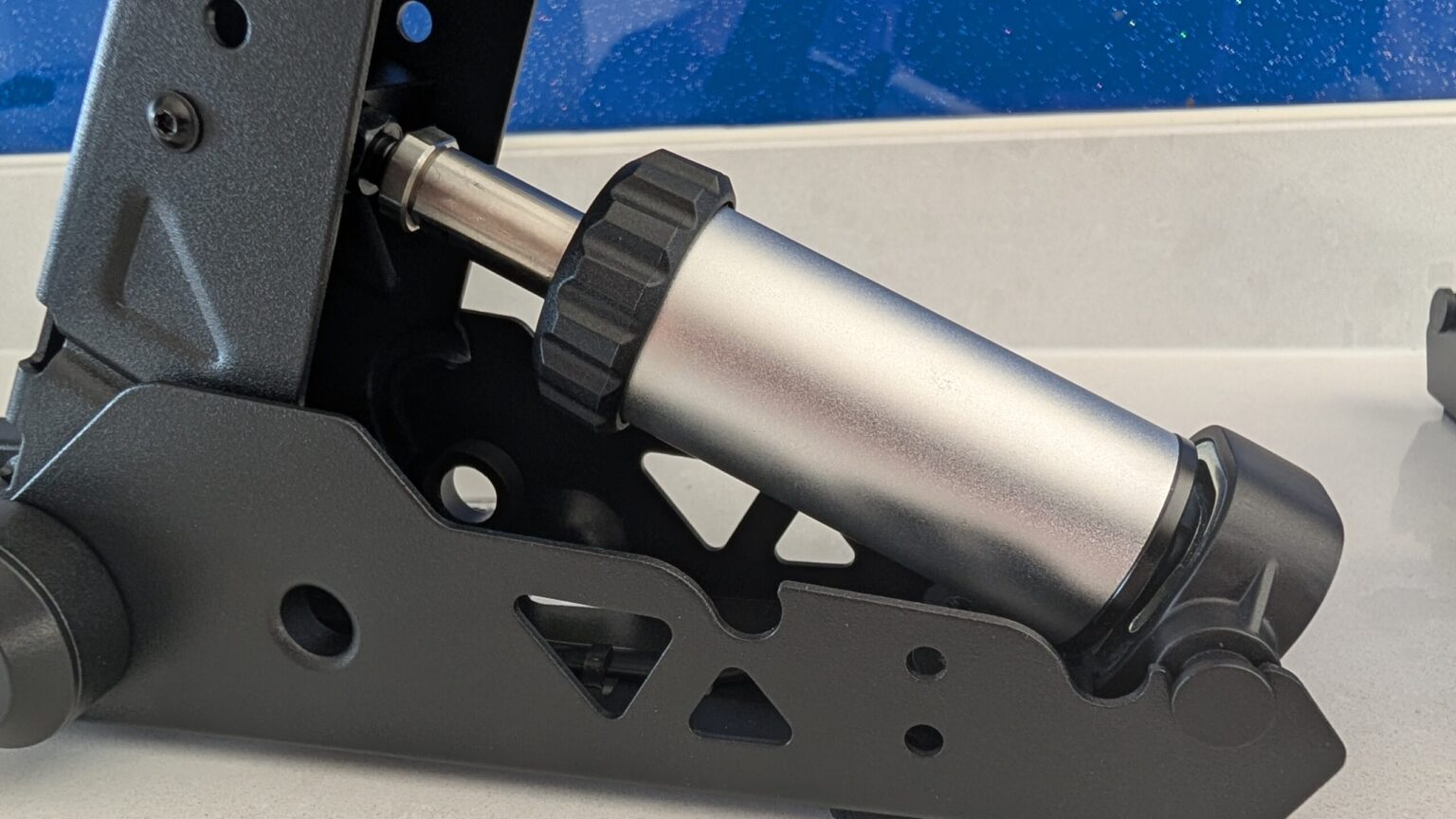 Close-up van een zwart metalen mechanisme met een zilveren cilinder en zwarte greep.