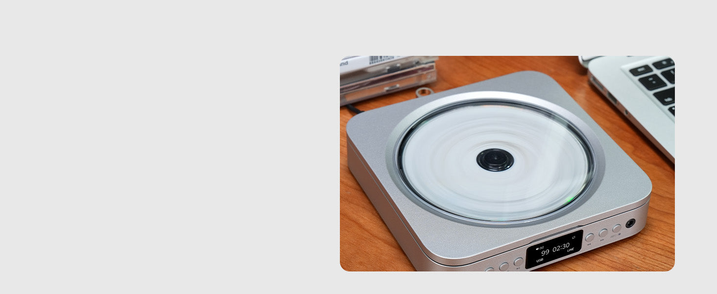 Zilveren CD-speler met draaiende CD, naast laptop op houten tafel.