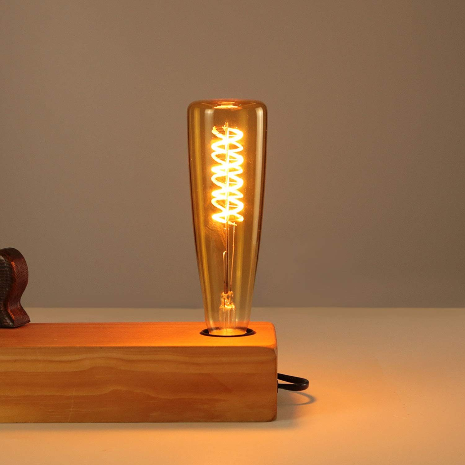 Eine Edison-Glühbirne mit Spiralwendel auf einem Holzsockel leuchtet warm.