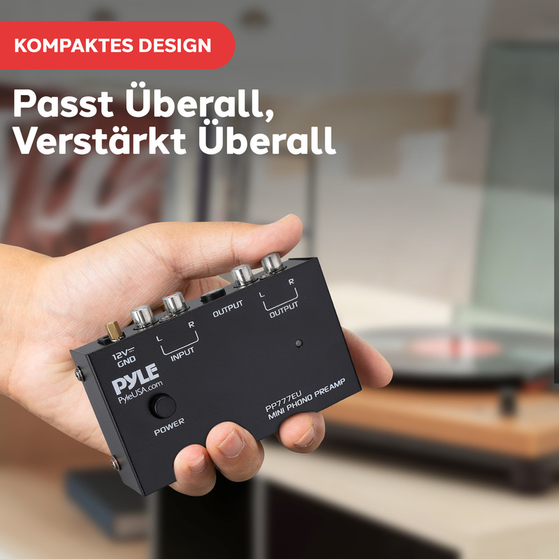 Hand hält schwarzen Mini-Phono-Vorverstärker mit Anschlüssen und Beschriftungen.