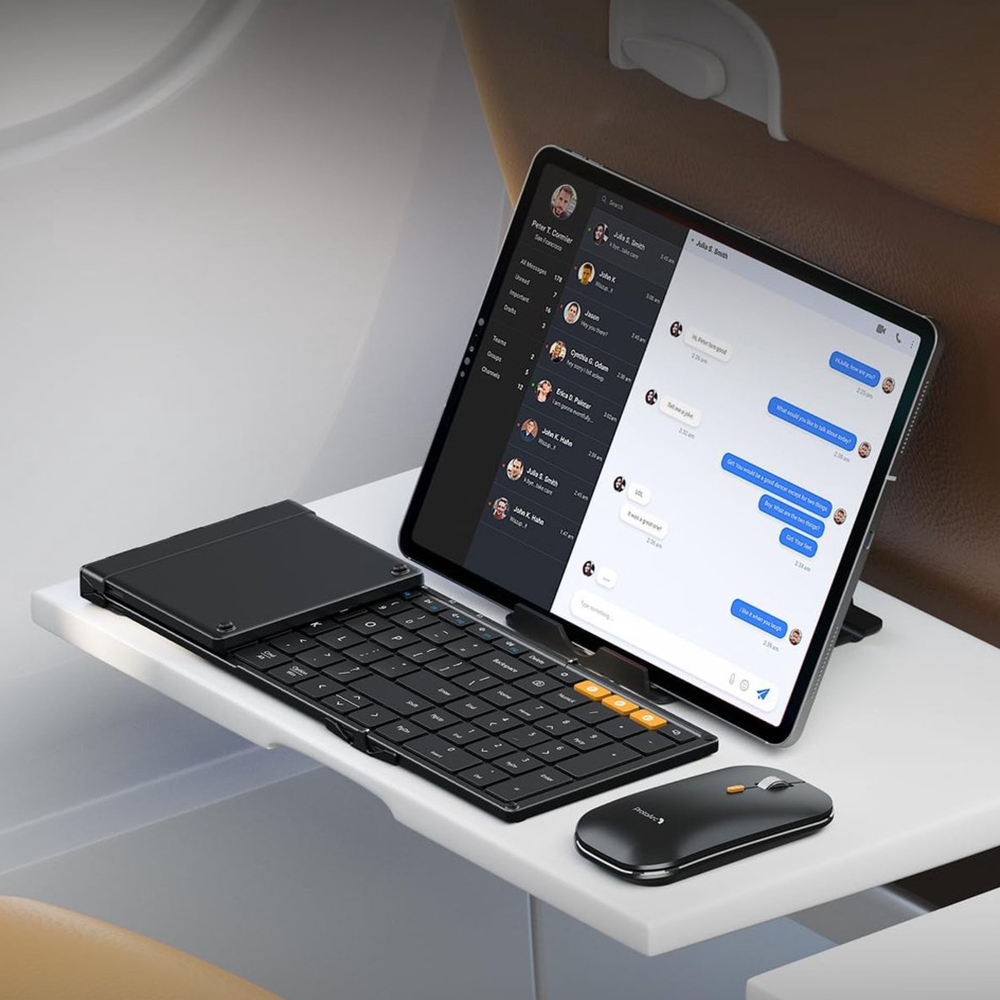 Un teclado, trackpad y ratón negros sobre una superficie blanca junto a una tablet mostrando un chat.