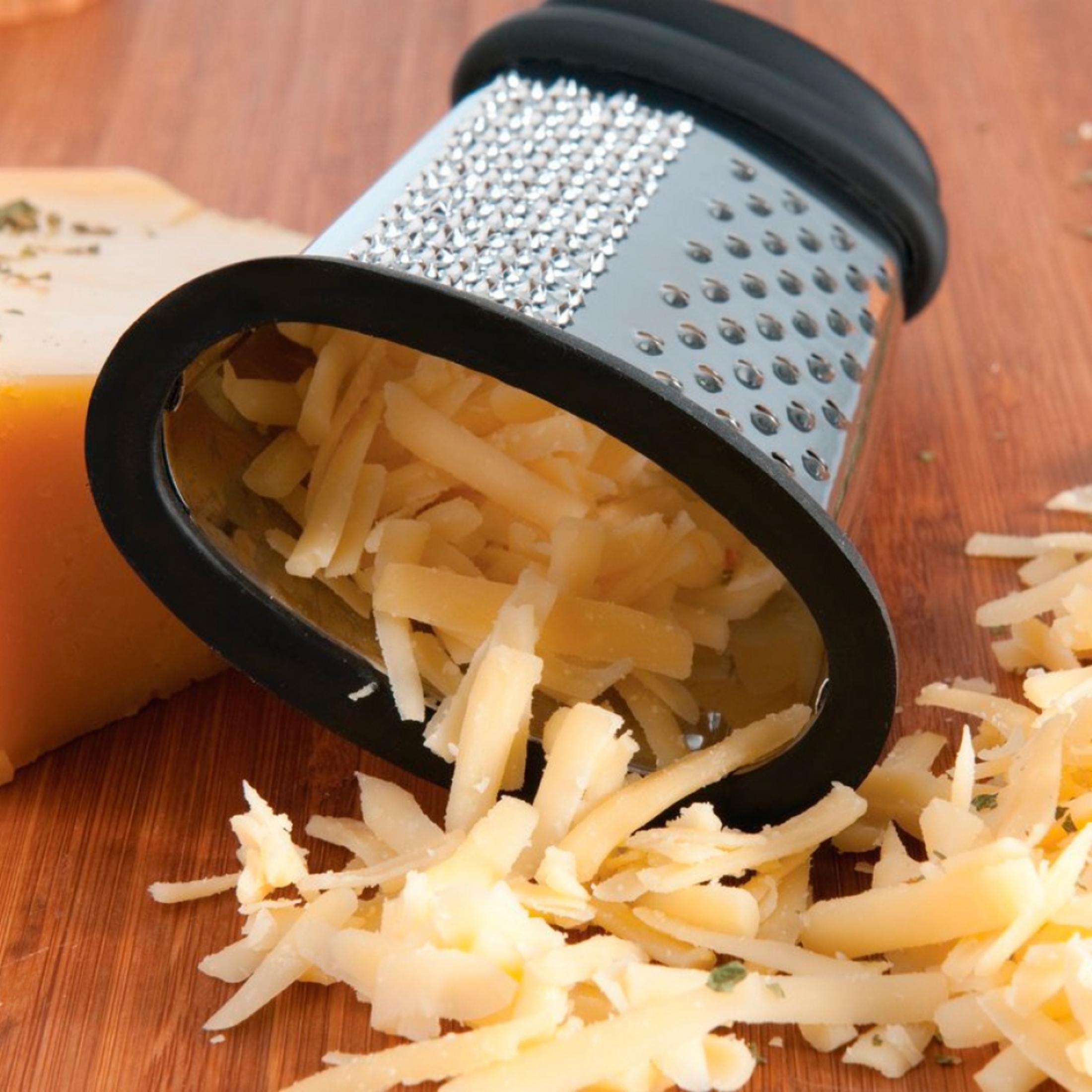 Una grattugia per formaggio su un tagliere di legno con formaggio grattugiato.
