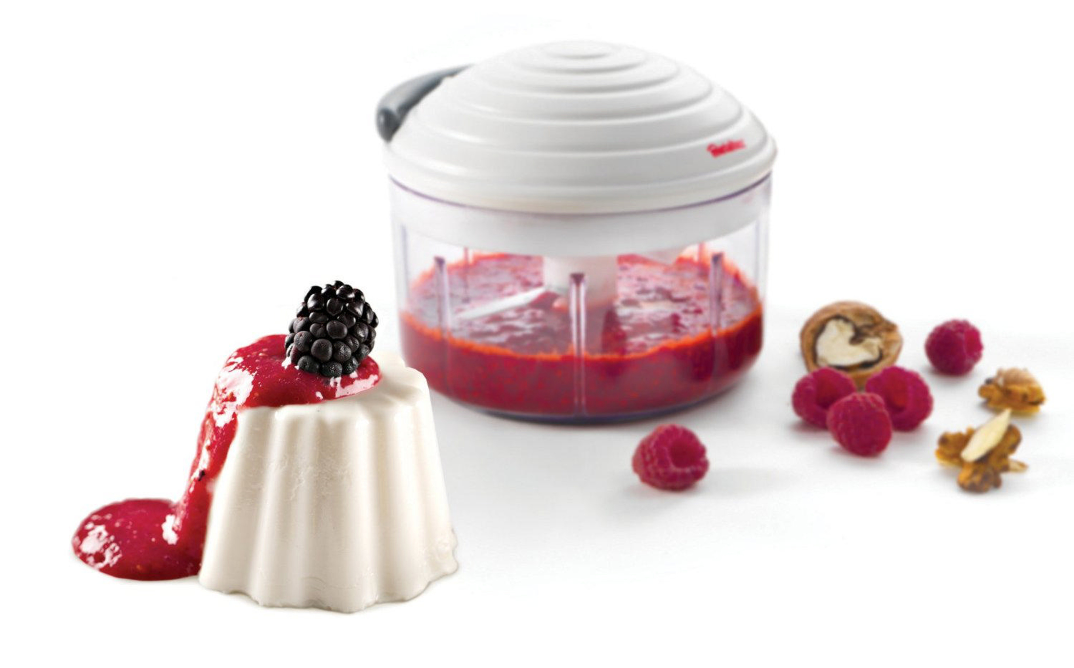 Panna cotta con salsa di frutti di bosco e mora, vicino a un tritatutto con purea.