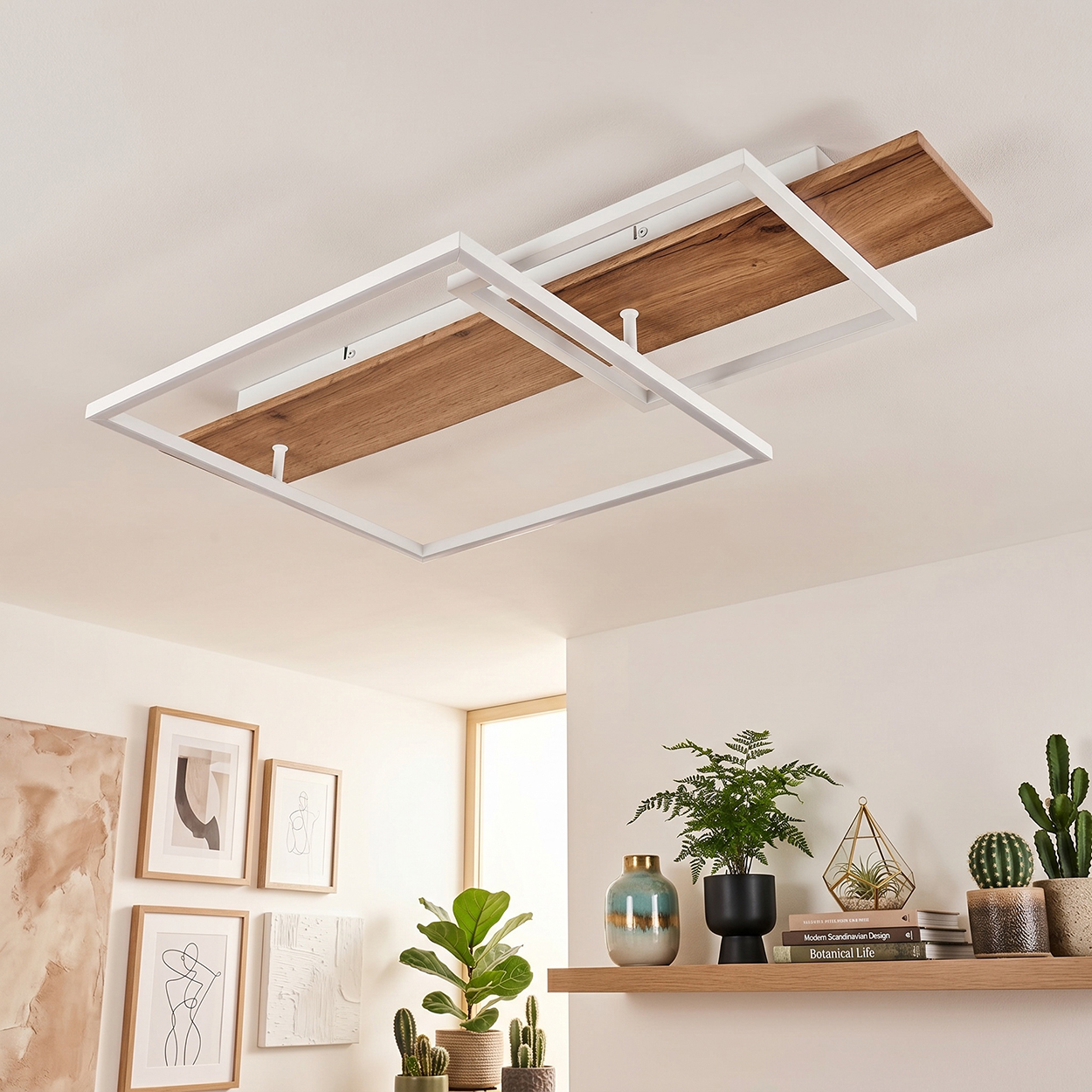 Moderne Deckenleuchte mit Holz und weißen Rahmen, daneben Bilder und Pflanzen.