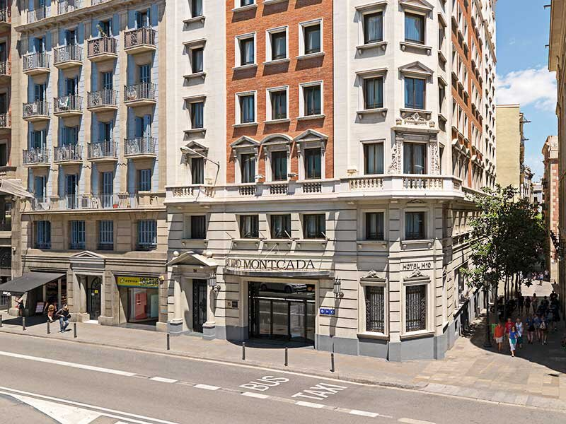 Un hotel con fachadas rojas y beige, balcones y ventanas, calle delante.