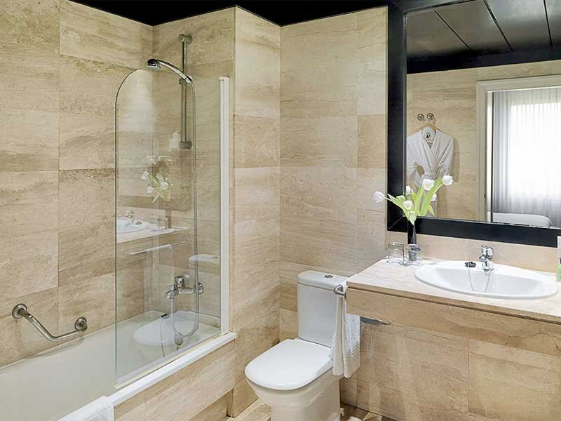 Un baño con bañera, inodoro, lavabo y espejo. Una bata cuelga del espejo.