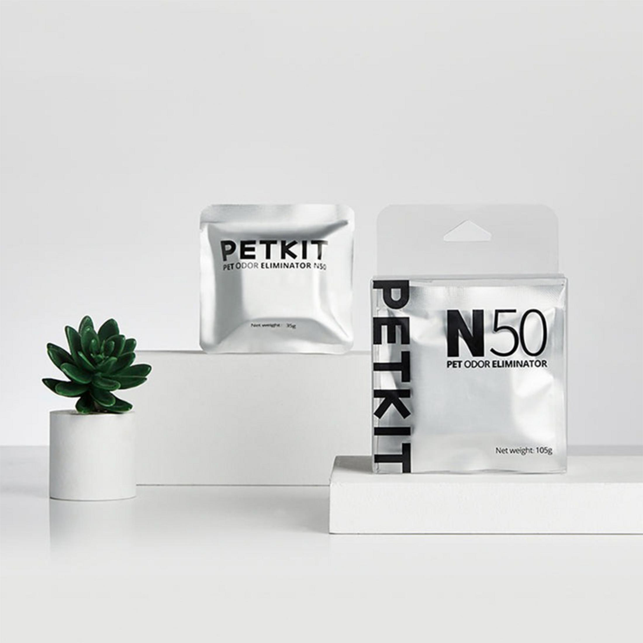 İki PETKIT koku giderici paketi ve saksıda yeşil bir bitki.