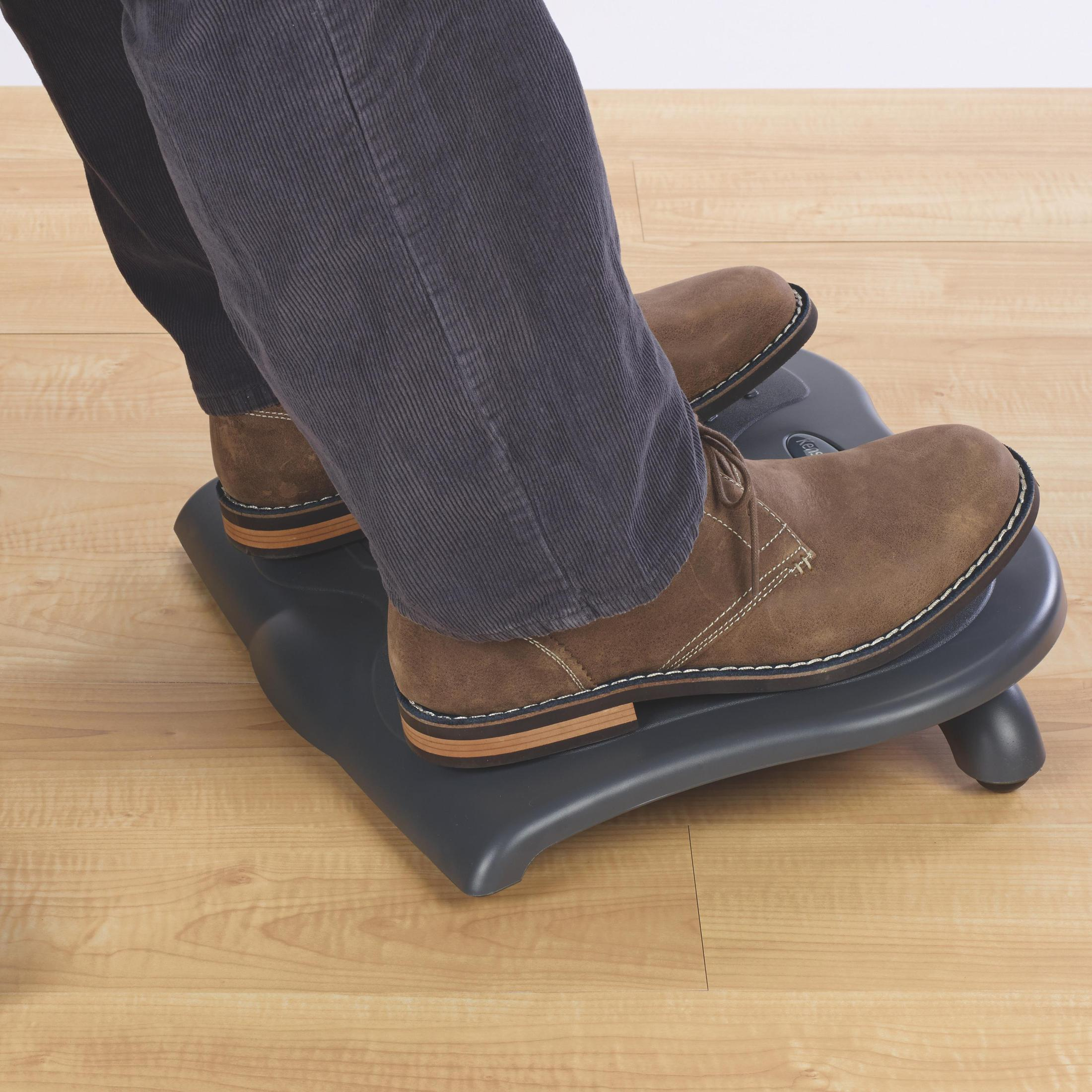 Füße in braunen Schuhen auf einer grauen Fußstütze auf Holzboden.