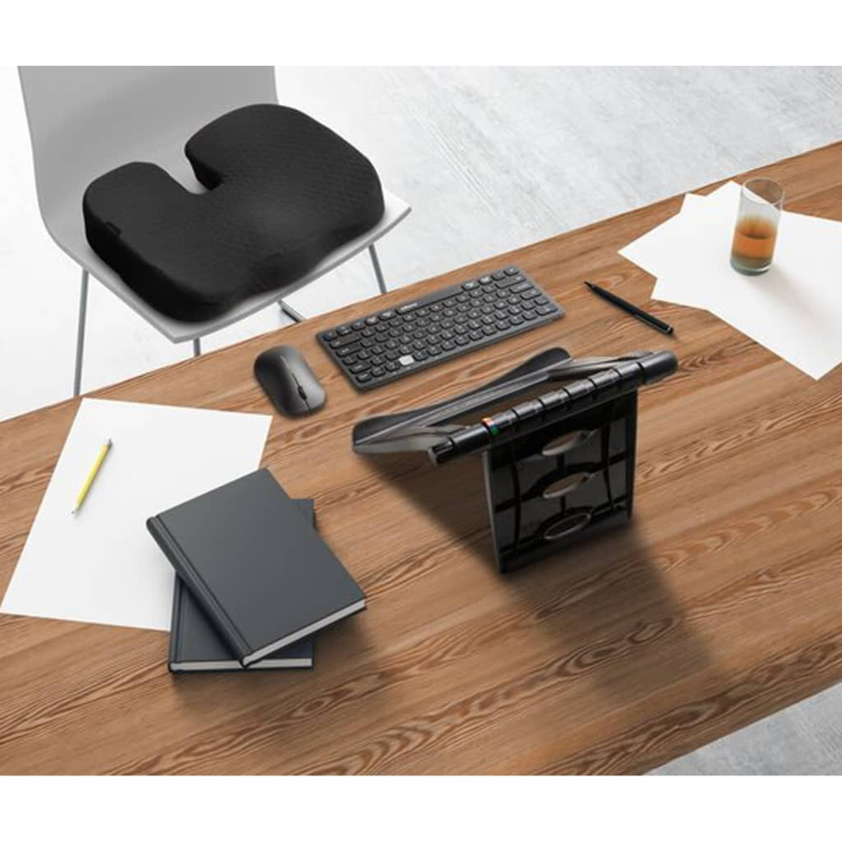 Ein schwarzes Sitzkissen auf einem Stuhl neben einem Schreibtisch mit Tastatur, Maus und Büchern.