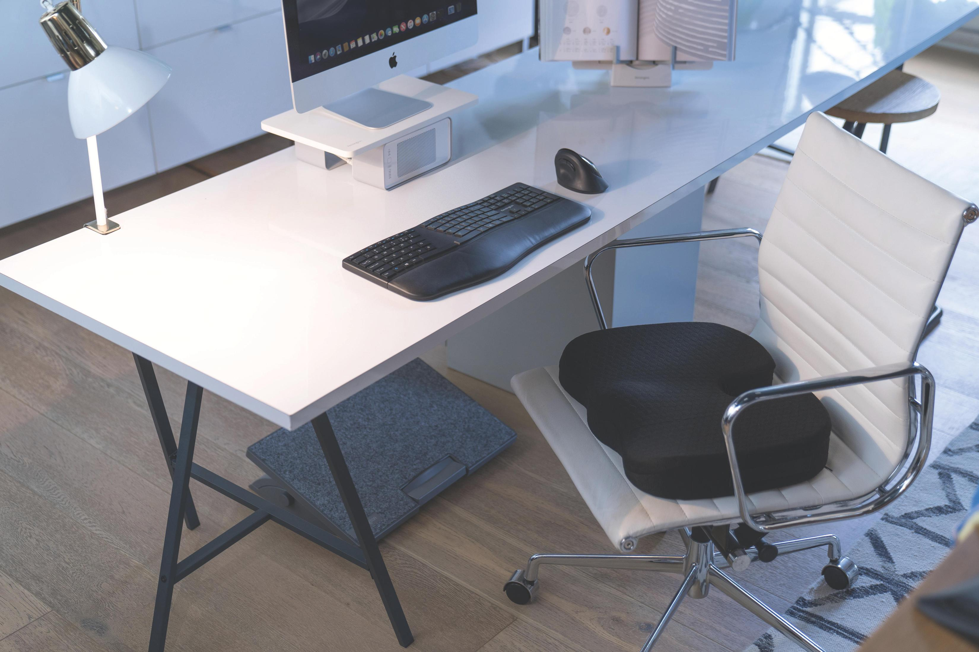 Ein weißer Schreibtisch mit einem iMac, Tastatur, Maus, Lampe und Bürostuhl.