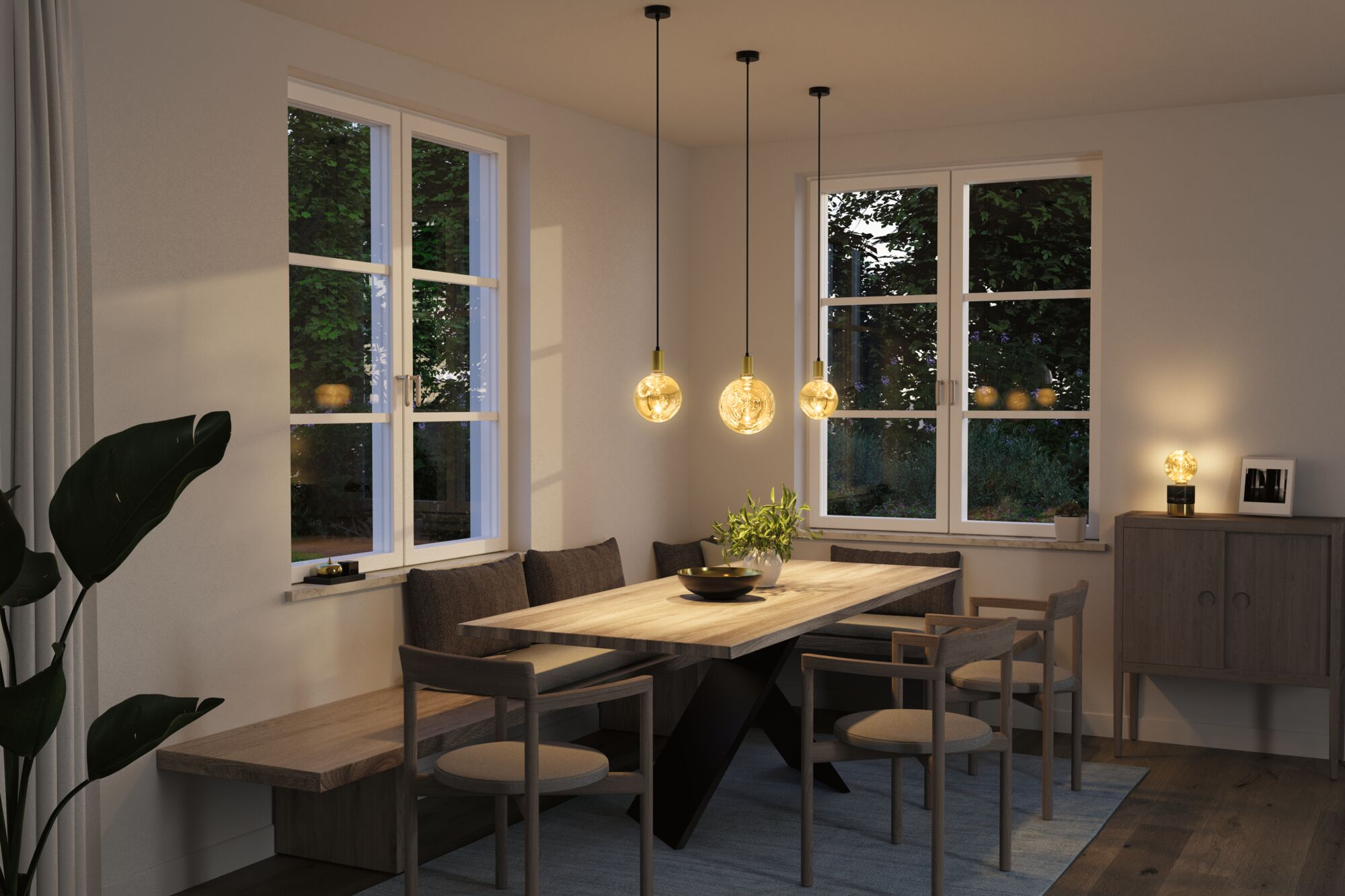 Ein Esszimmer mit Holztisch, Bank, Stühlen, Hängeleuchten und Fenstern.