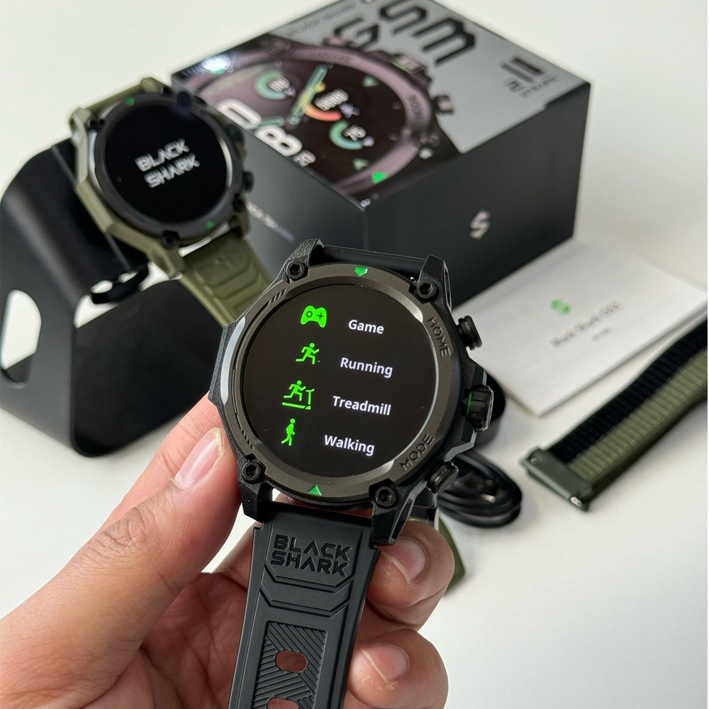 Una mano sostiene un smartwatch que muestra modos deportivos: Juego, Correr, Cinta y Caminar.
