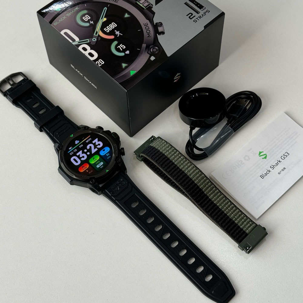 Smartwatch negra con cable de carga, correa extra y manual.