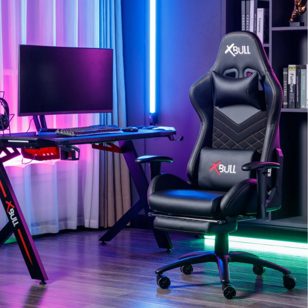 Una sedia da gaming nera con poggiapiedi e una scrivania con monitor.