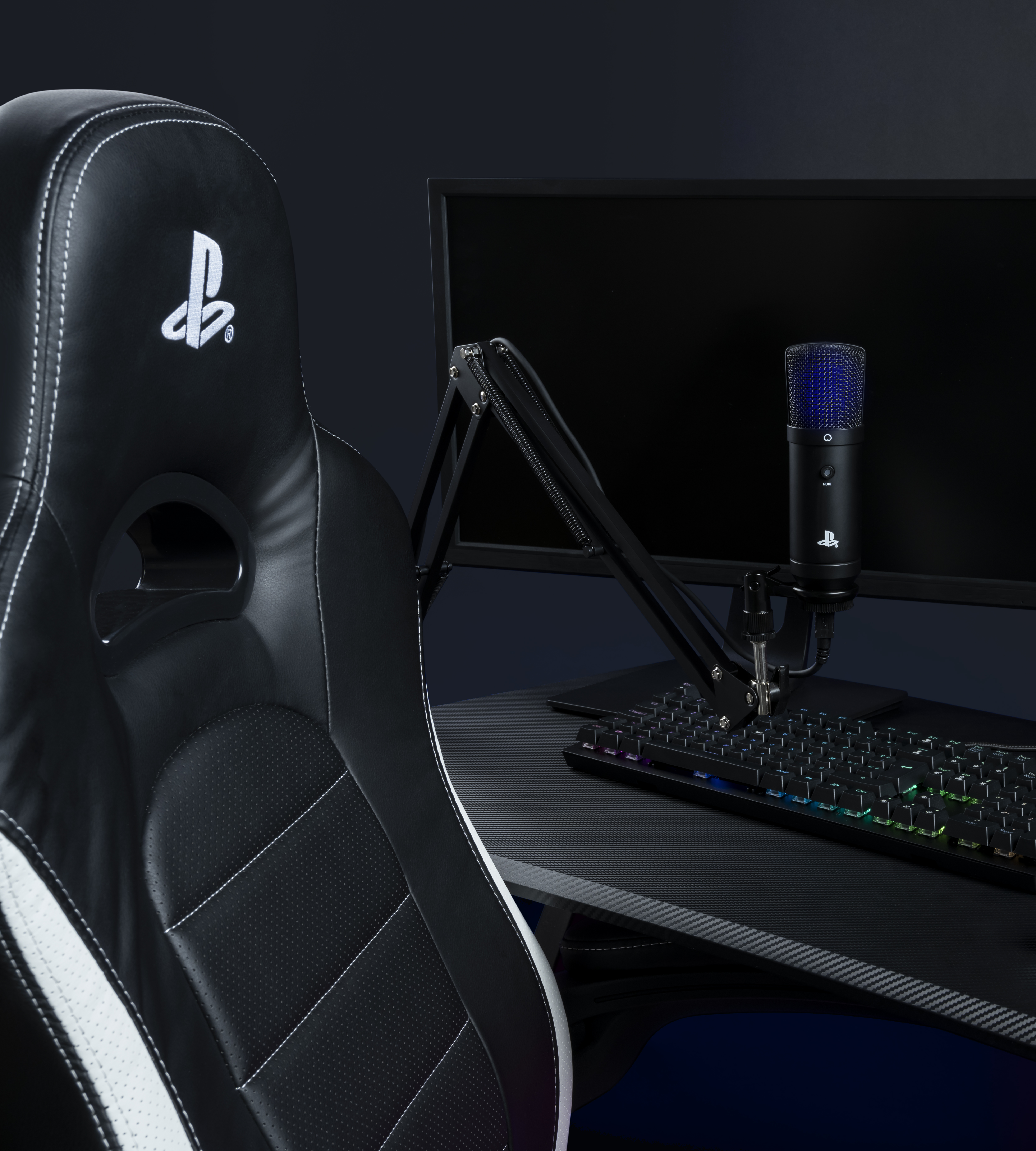 Ein schwarzer Gaming-Stuhl mit PlayStation-Logo, Tastatur und Mikrofon auf einem Schreibtisch.