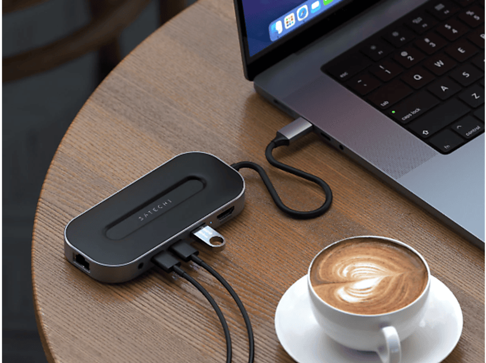 Ein Satechi-Hub verbindet einen Laptop mit einer Kaffeetasse auf einem Holztisch.