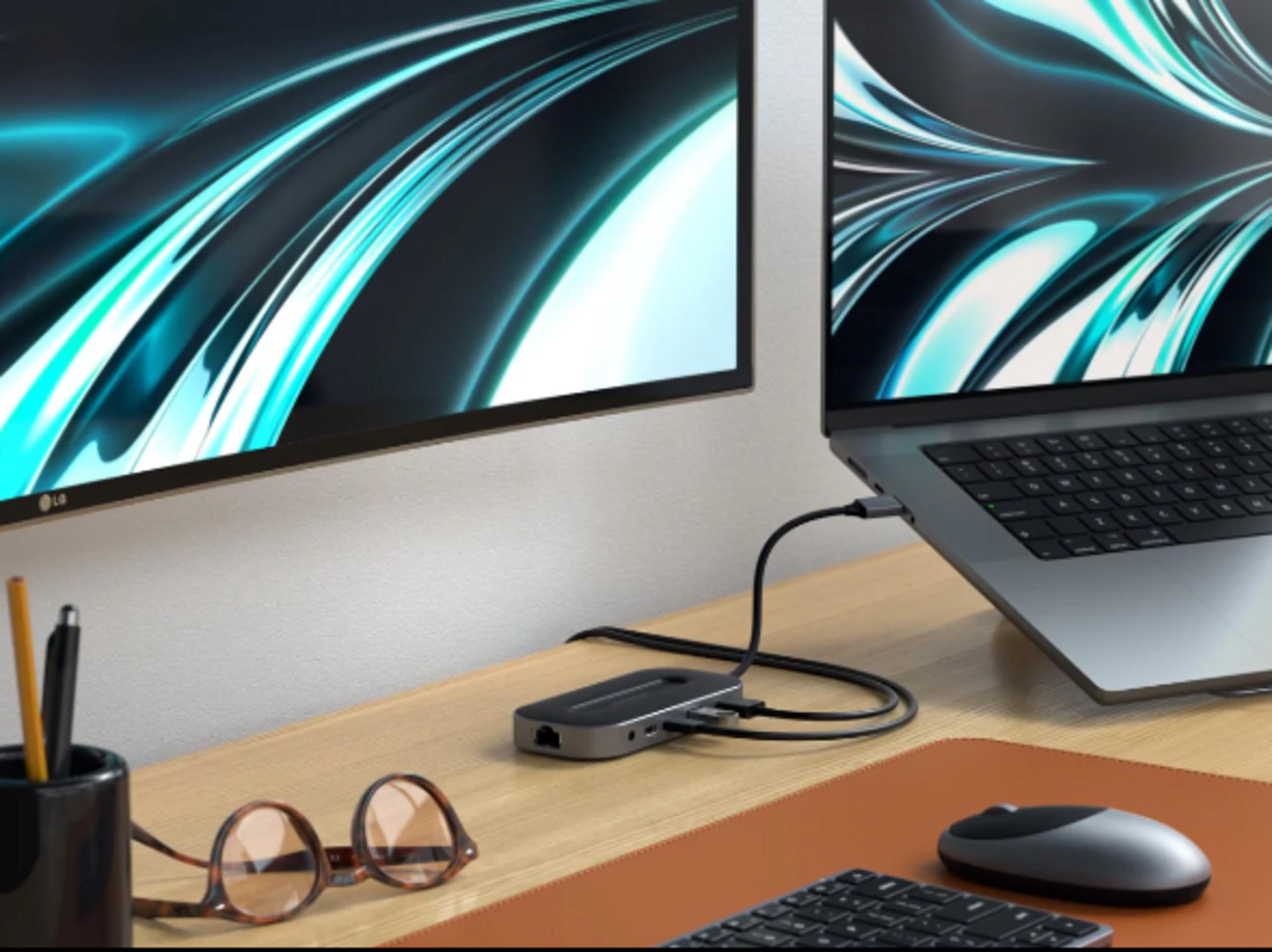Ein Laptop, ein Monitor, ein Dock, Brille, Maus und Tastatur auf einem Schreibtisch.