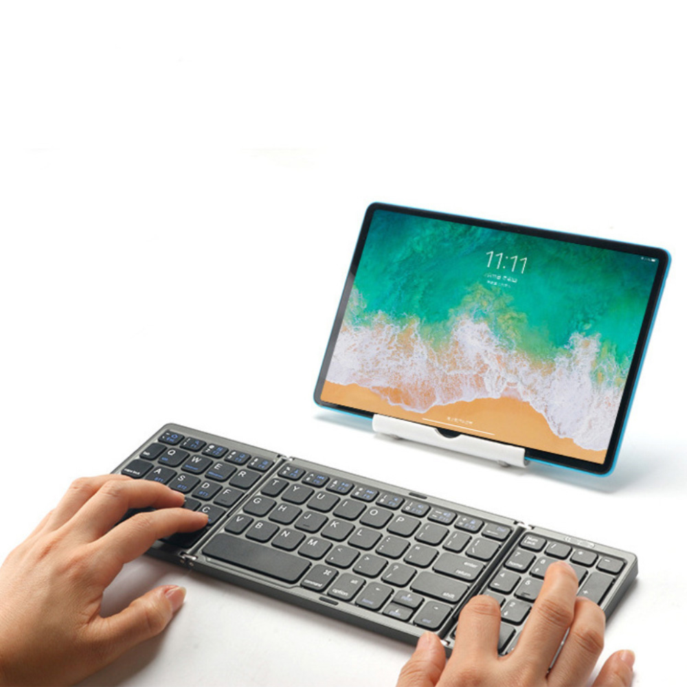 Hände tippen auf einer grauen faltbaren Tastatur vor einem Tablet mit Strandmotiv.
