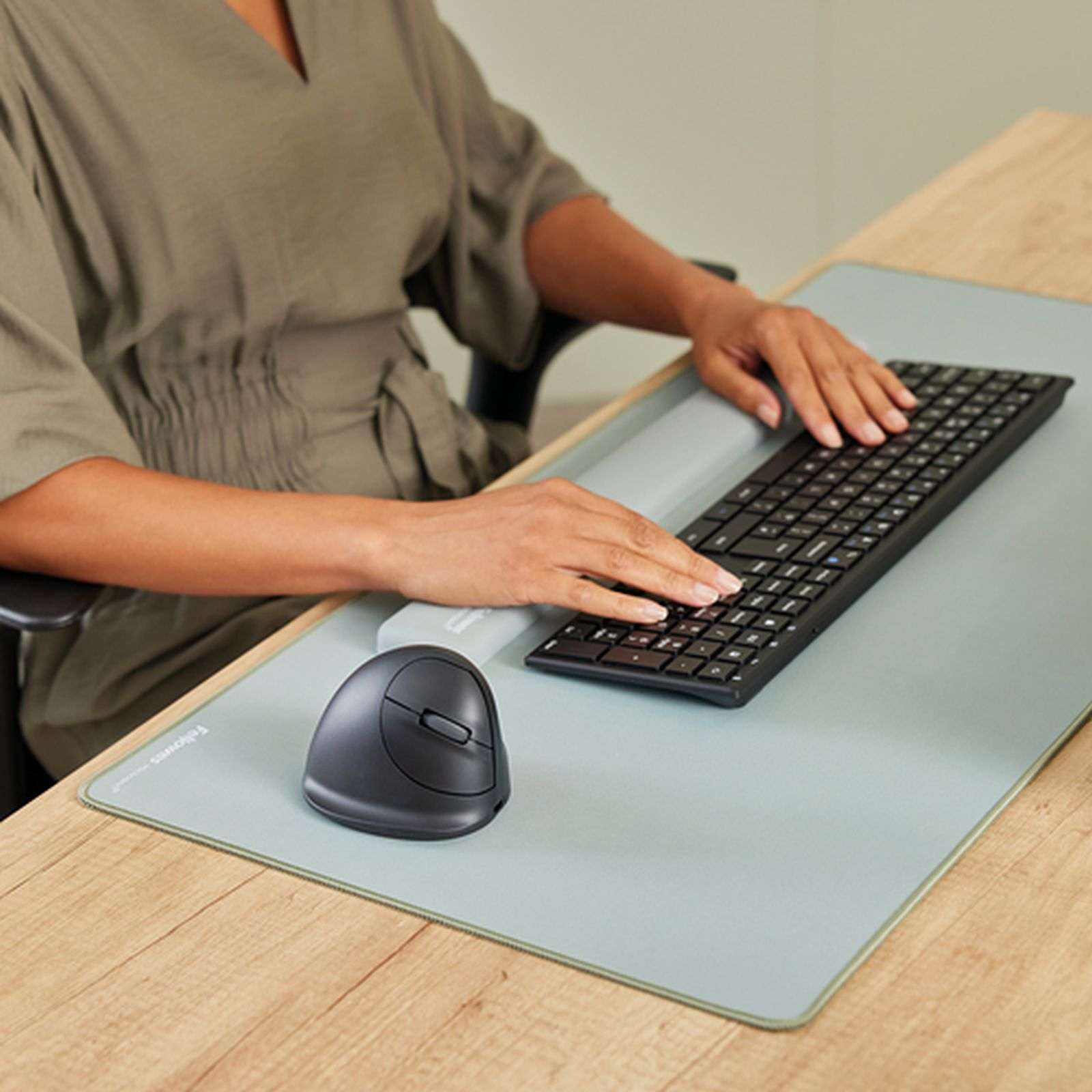 Eine Person tippt auf einer Tastatur, daneben eine Maus und eine Handgelenkauflage.