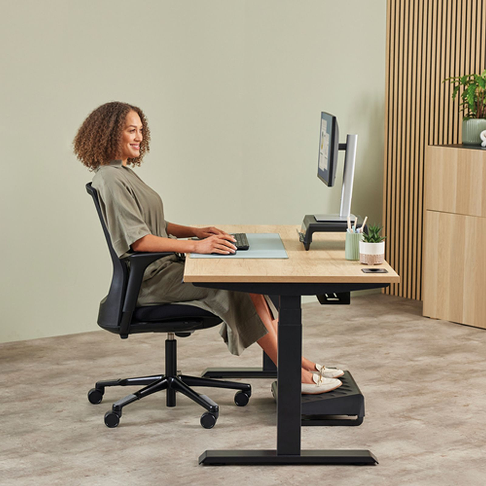 Eine Frau sitzt an einem Schreibtisch mit einem Computer und einem Fußhocker.