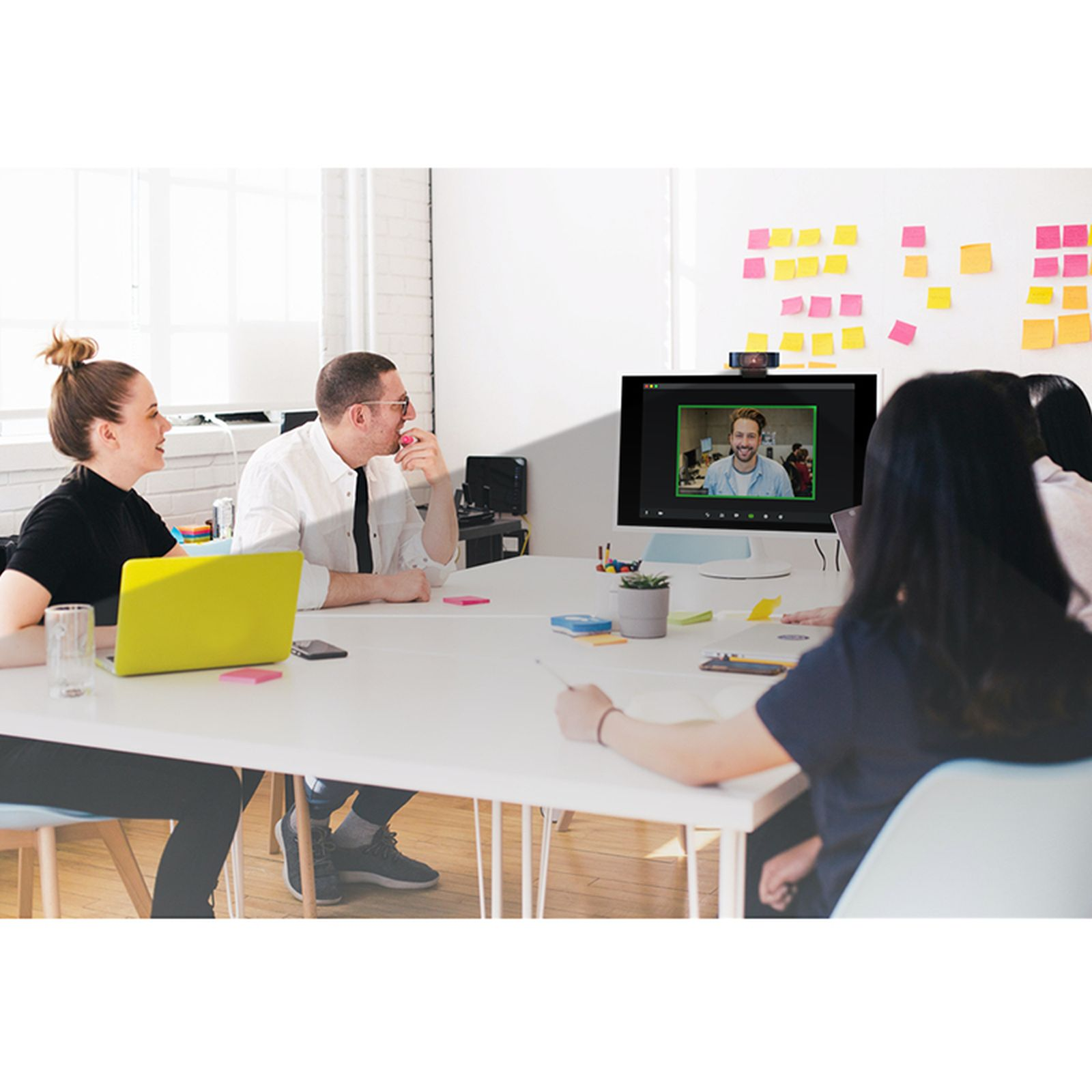 Persone in un ufficio in una videochiamata con un uomo sullo schermo.