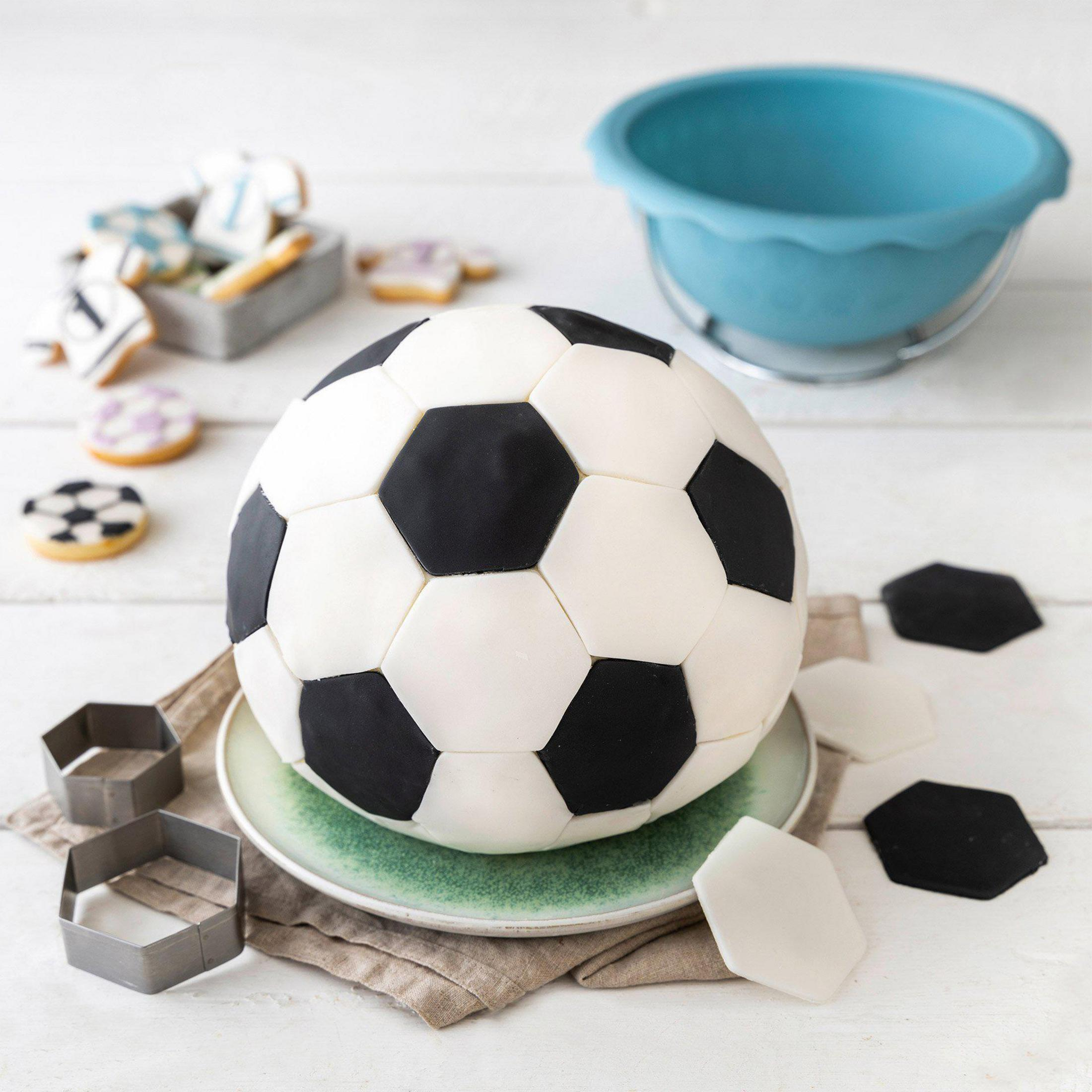 Fußballkuchen auf grünem Teller mit Keksen und Schüssel im Hintergrund.