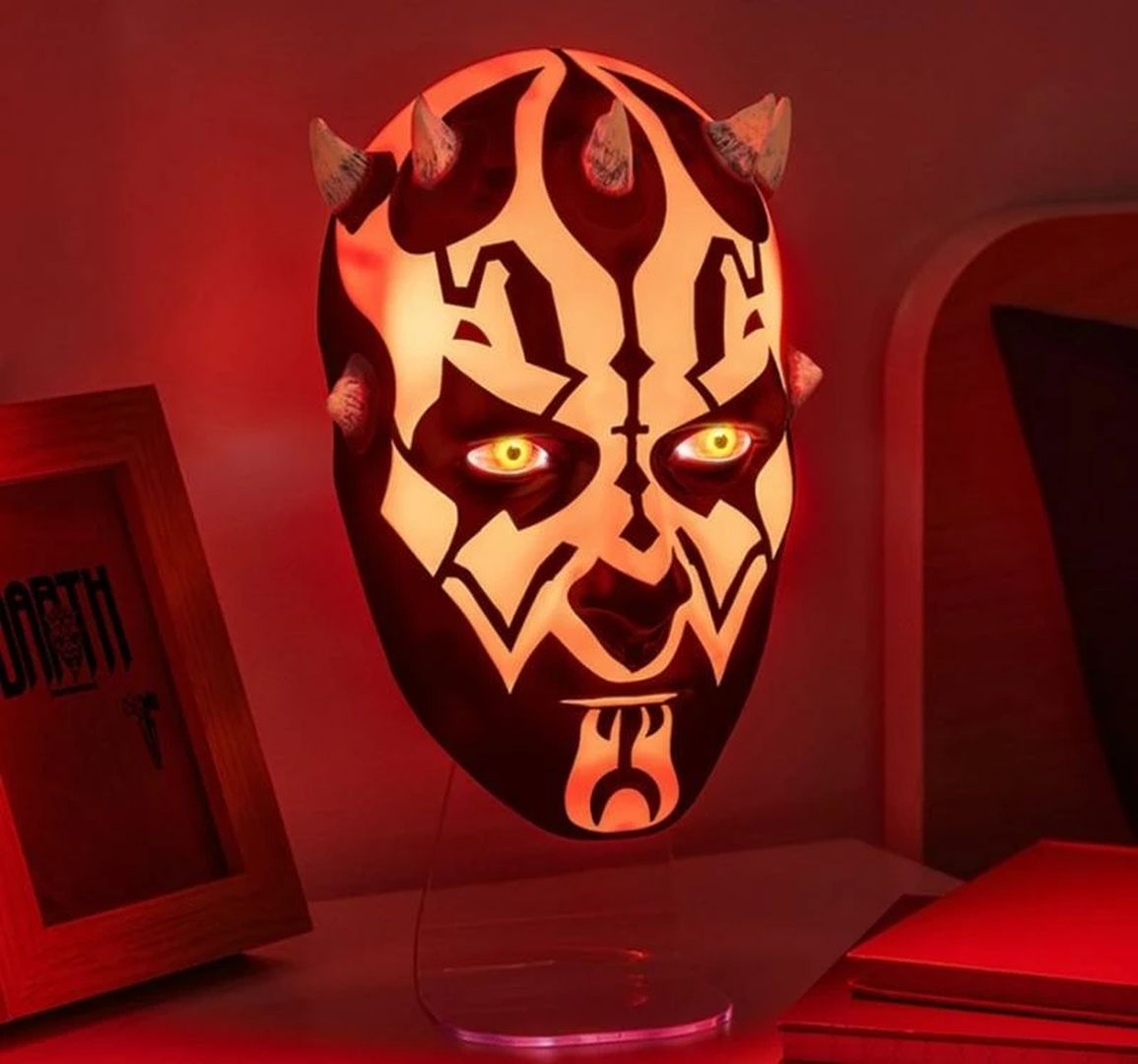 Una máscara brillante de Darth Maul con ojos amarillos y cuernos está sobre un soporte.