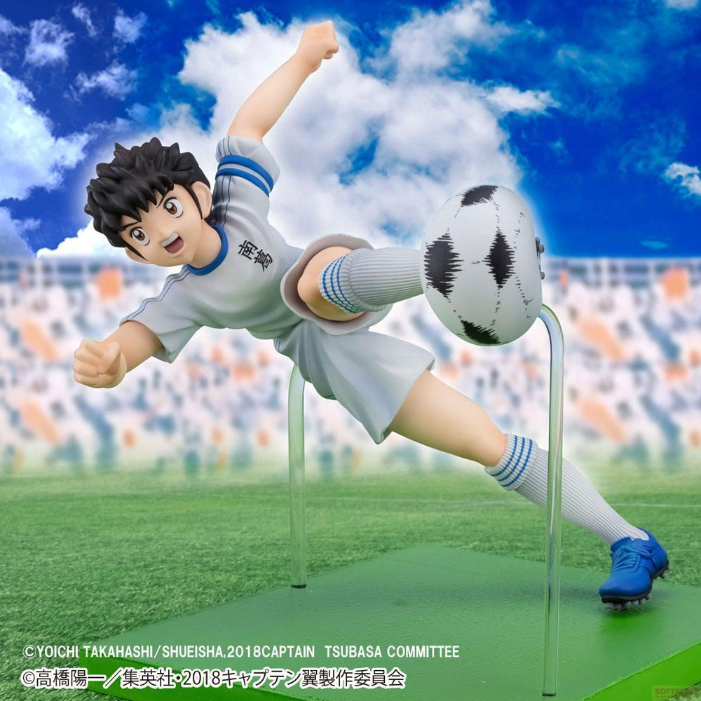 Eine Figur eines Fußballspielers im Trikot, der den Ball tritt, mit blauem Himmel und Wolken.