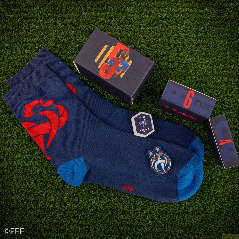 Blaue Socken mit rotem Hahn-Logo, kleine Schachteln mit Nummern, auf grünem Kunstrasen.
