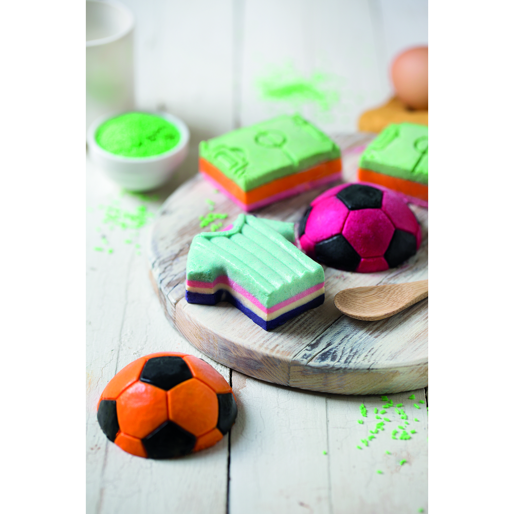 Bunte Fußball-Badebomben in Trikot-, Ball- und Kastenform auf Holzbrett.