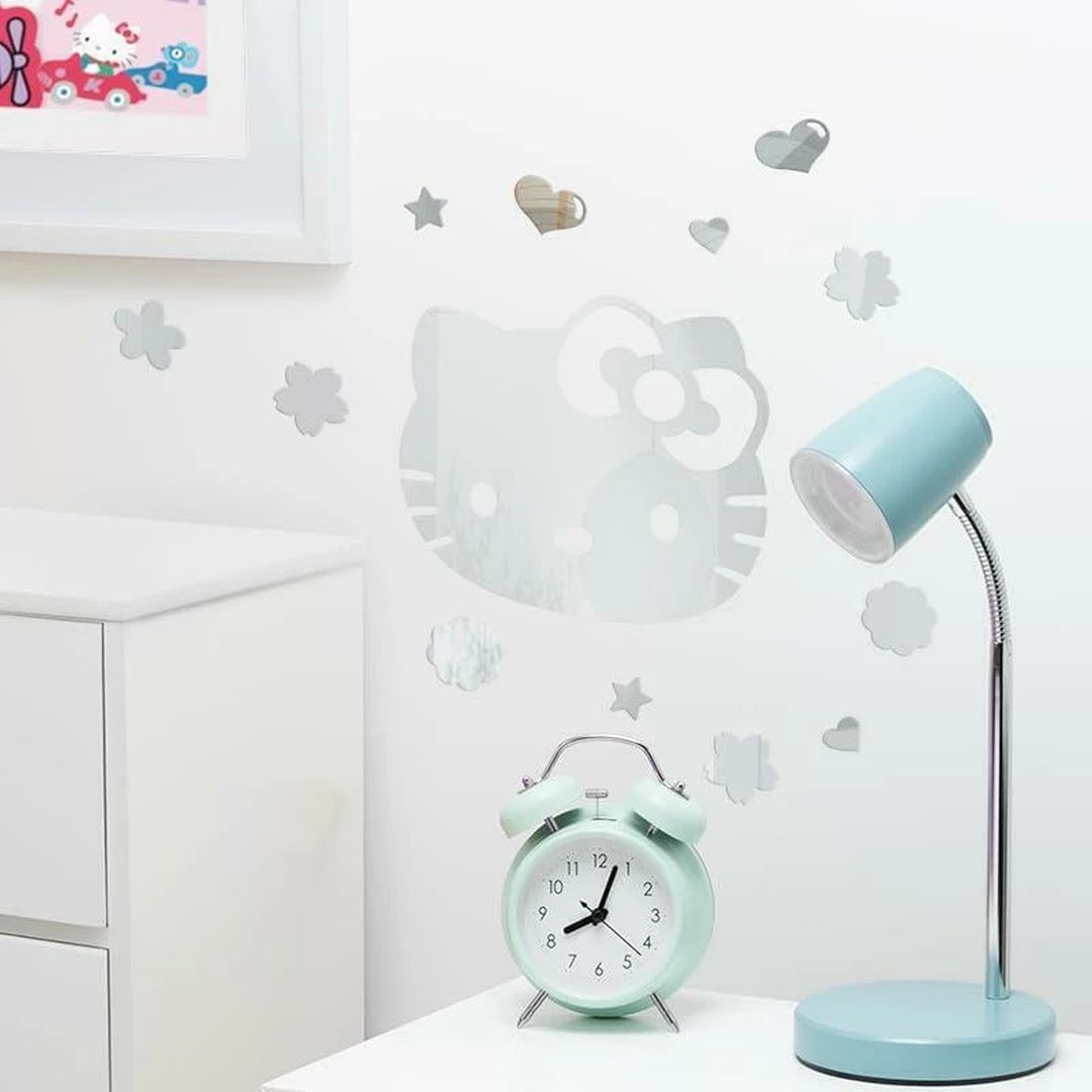Un despertador azul claro junto a una lámpara de escritorio, pegatinas de Hello Kitty en la pared.