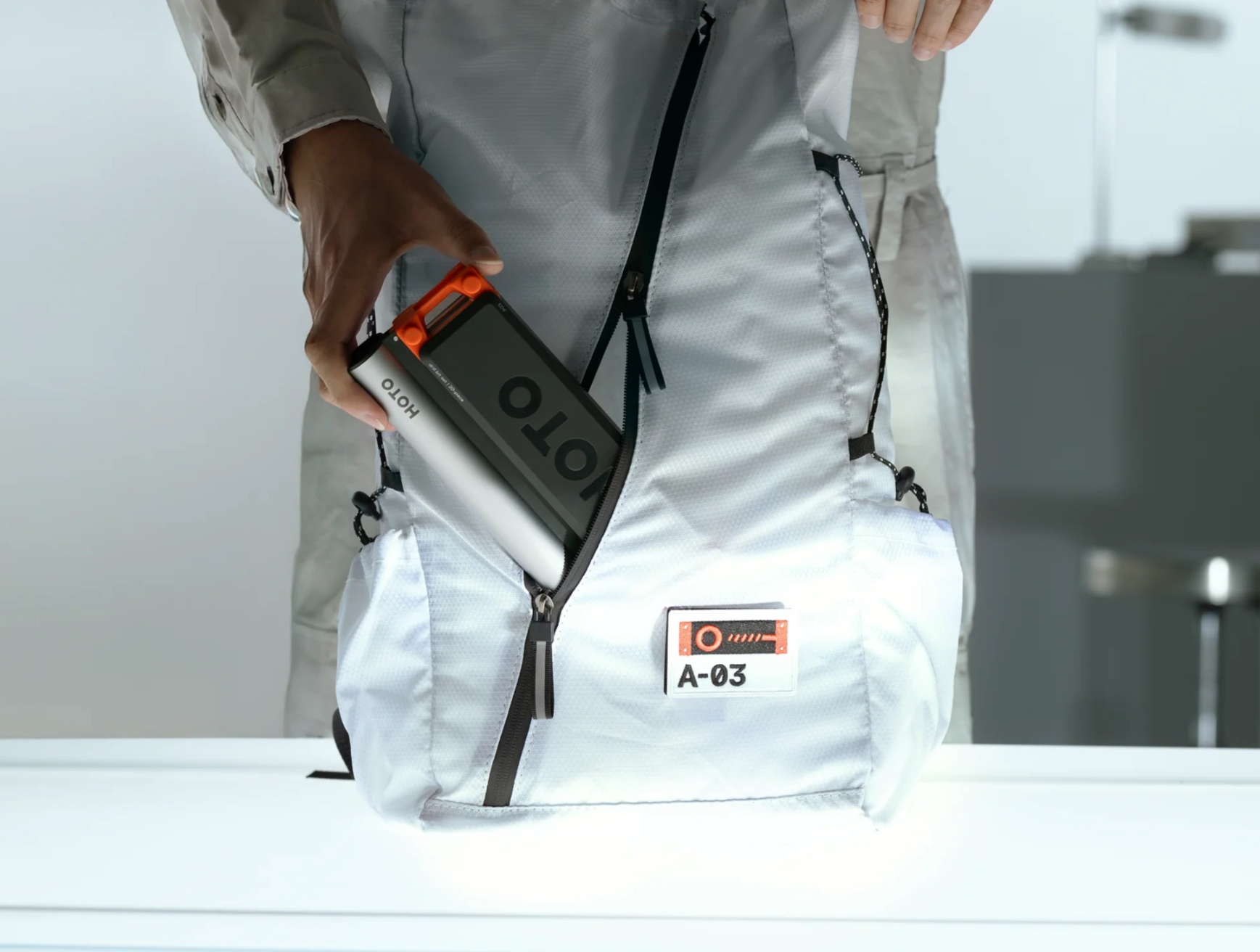 Osoba wkłada powerbank i urządzenie do białego plecaka.