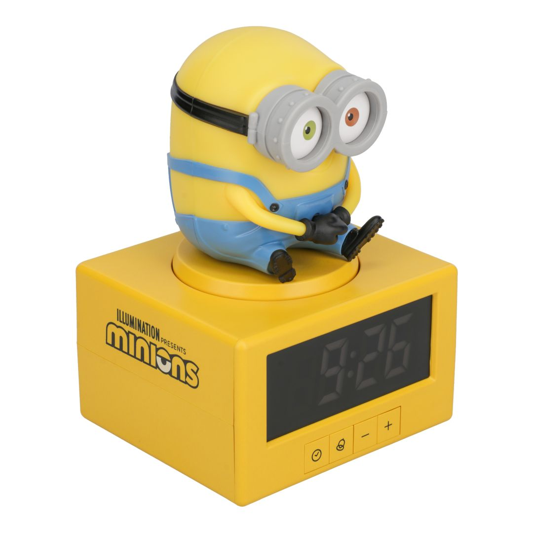 Żółta figurka Minionka siedzi na żółtym budziku pokazującym 9:26.