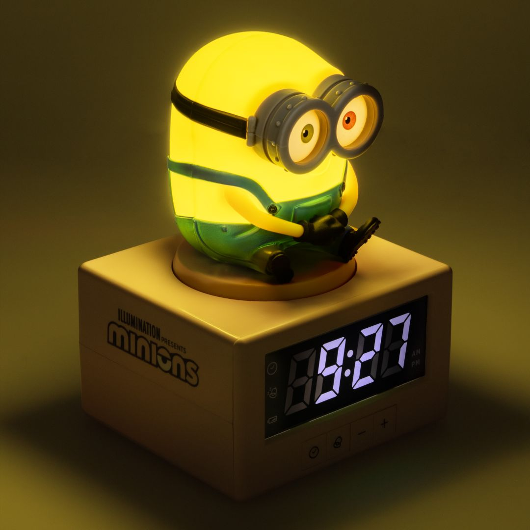 Żółta postać Minion siedzi na białym budziku wyświetlającym 09:27.